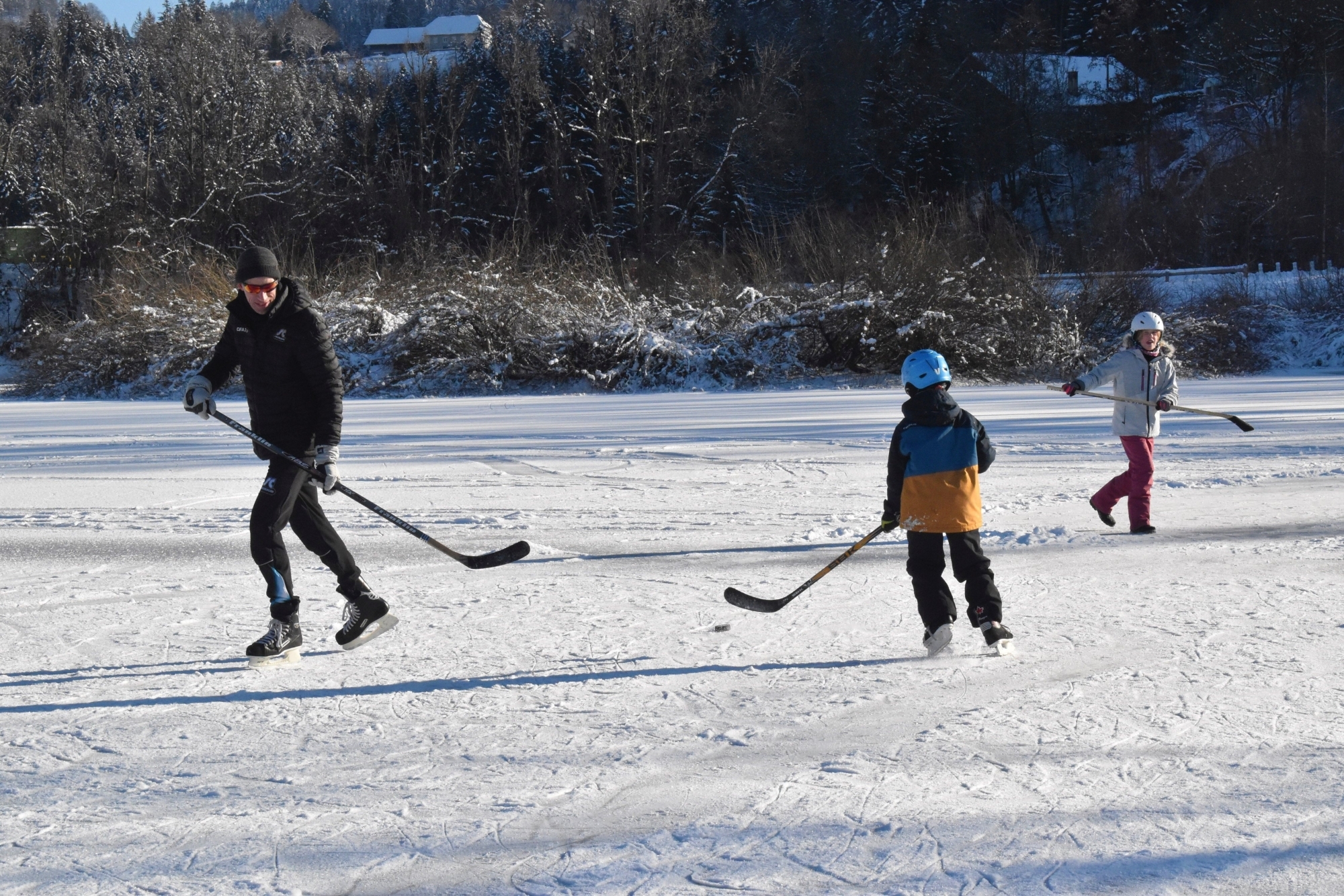 Petite famille en train de profiter du lac des Brenets gelé pour y jouer au hockey sur glace lorsque la surface était encore une bonne patinoire bien solide.