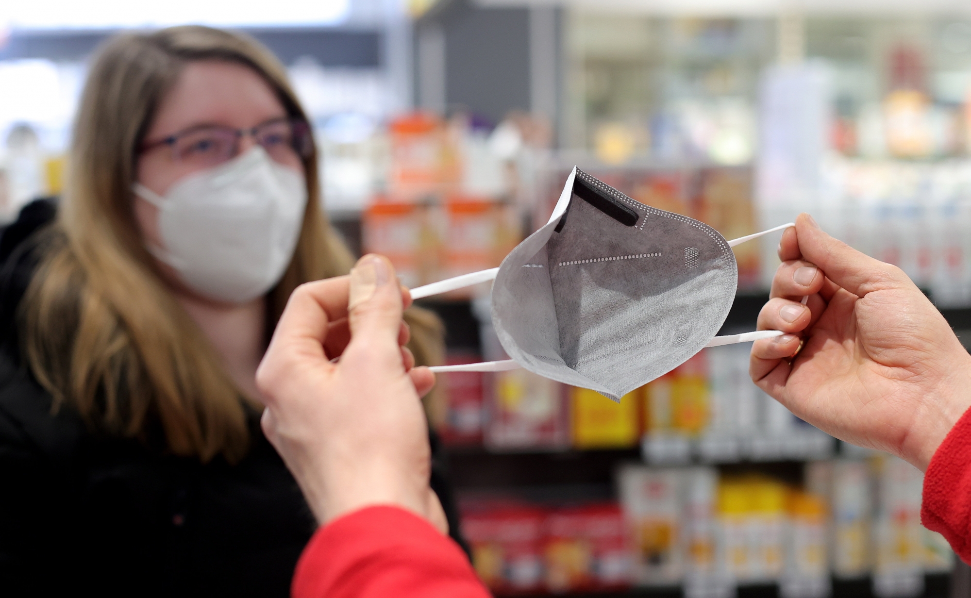 epa08958384 Pharmacist Stephan Neuhaus demonstrates the usage of a FFP2 protective mouth-nose mask with grey fleece to a customer at the Baeren pharmacy in Dortmund, Germany, 22 January 2021. In Germany, medical face masks will in future have to be worn on public transport, when shopping and even at religious services. To protect themselves more effectively, surgical masks or mouth-nose protection with the standards KN95/N95 or FFP2 will be required. People over 60 and people with certain chronic diseases will receive two vouchers for six FFP2 masks each from their health insurers and can redeem them at the pharmacy for a fee of two euros each.  EPA/FRIEDEMANN VOGEL