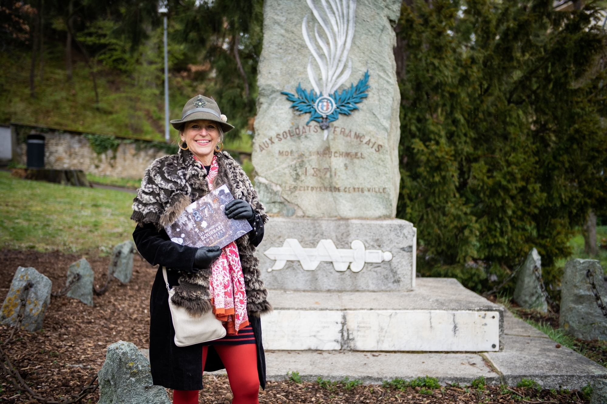 Dominique Wacker-Cao avec son livre devant le monument des Bourbakis à Neuchâtel, à l'emplacement de l'ancien cimetière du Mail.