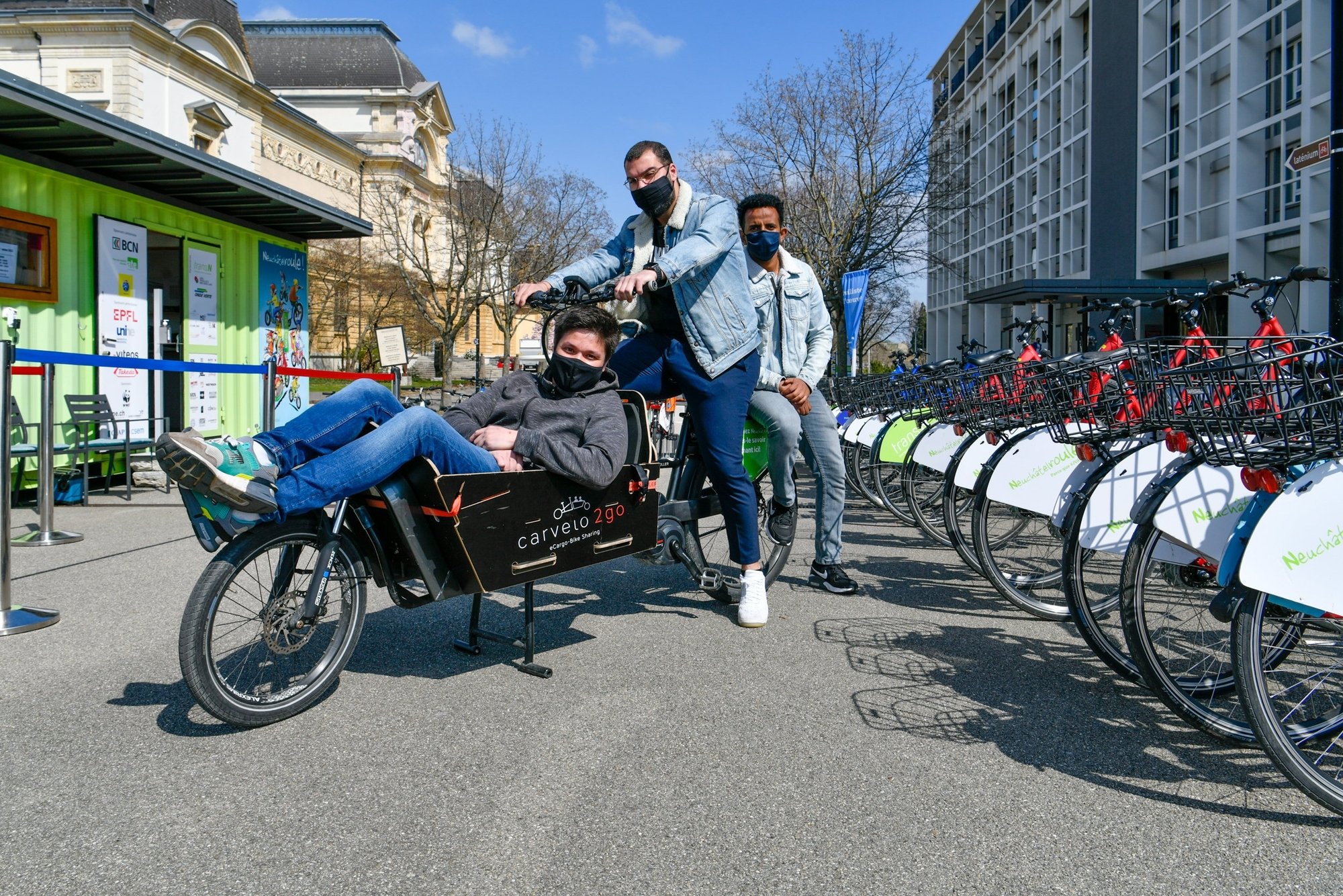 Ken Humbert, Newroz Genç et Dawit Andemeskel (de g. à dr.) posent avec un vélo-cargo électrique devant la station du port.