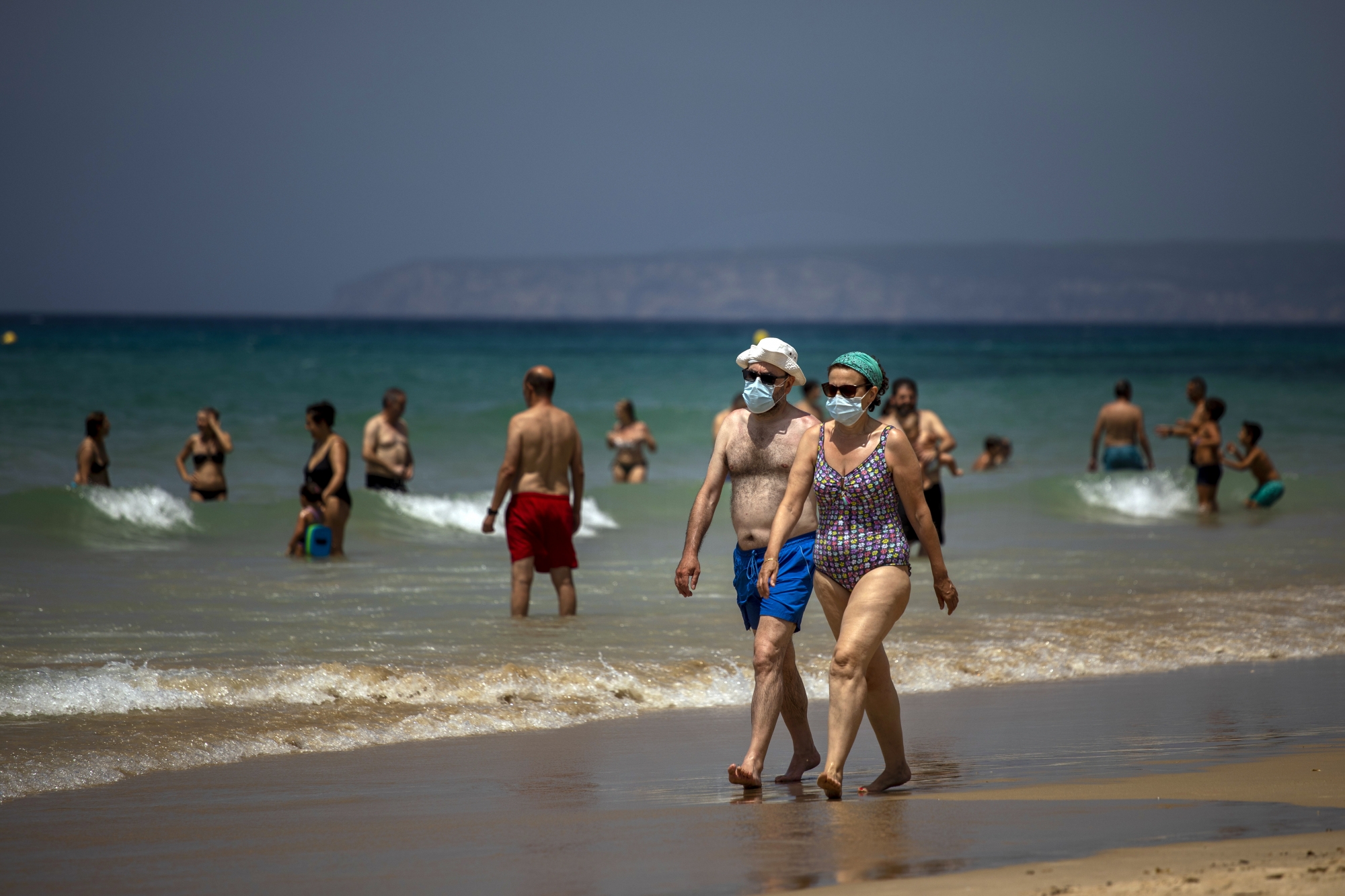 A couple wearing face masks walk along the shore in a beach in Cadiz, south of Spain, on Tuesday, July 21, 2020. (KEYSTONE/AP Photo/Emilio Morenatti)