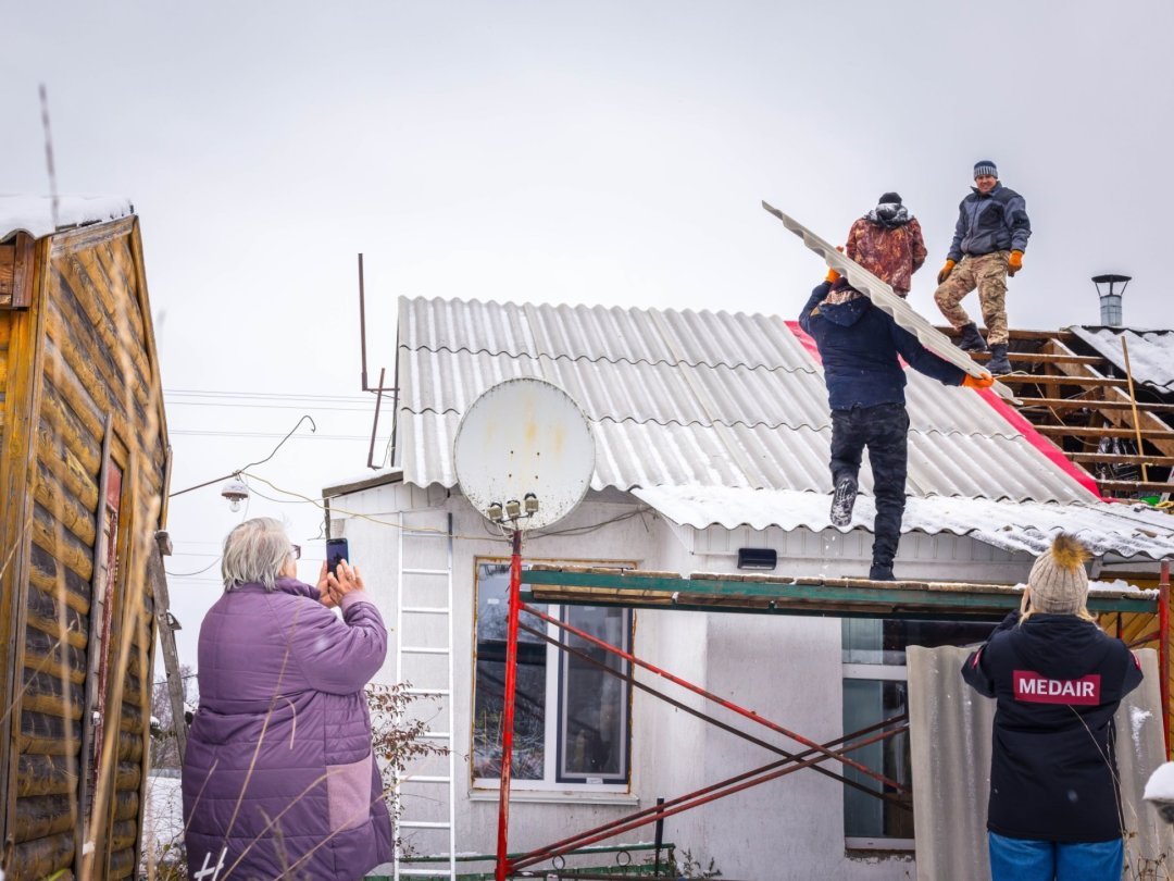 Plusieurs couvreurs ukrainiens engagés par l'ONG Medair installent un toit sur la maison de Lyudmyla (à gauche). Agée de 69 ans, elle vivait sans toiture depuis mars 2022 et l'attaque de la Russie.