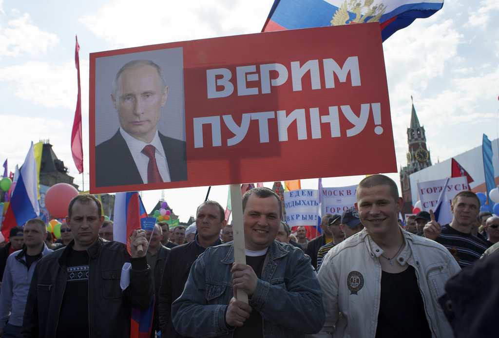 People holding Russian flags and posters march during the May Day celebration at the Red Square in Moscow, Russia, on Thursday, May 1, 2014. According to official reports about one hundred thousand people took part in the first May Day demonstration at the Red Square since the fall of the Soviet Union. The placards read: "We Believe in Putin, foreground," and "We will spend vacation in Crimea, background,." (AP Photo/Ivan Sekretarev)