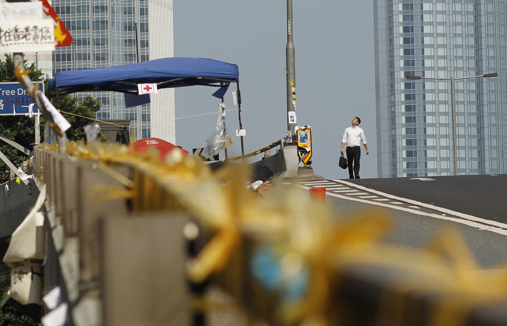 A businessman walks through the pro-democracy student protesters' thinly occupied areas surrounding the government complex in Hong Kong, Tuesday, Oct. 7, 2014. Student-led protests for democratic reforms in Hong Kong continued to shrink Tuesday morning but a few hundred demonstrators remained camped out in the streets, vowing to keep up the pressure until the government responds to their demands. (AP Photo/Wally Santana)