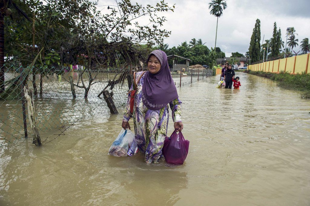 epa04536696 A women walks through the floodwaters near Rantau Panjang district of Kelantan state, 400 km north-east of Kuala Lumpur, Malaysia, 21 December 2014. Floods worsened in north-east Malaysia on 21 December due to heavy rains, the number of people who were evacuated in the state of Kelantan rose to 21,868 from more than 15,000 on 20 December, as evacuees in other areas began to return home amid improving weather, local authorities said.  Four fatalities were previously reported.  EPA/STR