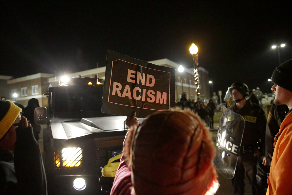A protester holds up a sign in front of the Ferguson Police Department Tuesday, Nov. 25, 2014, in Ferguson, Mo. Missouri's governor ordered hundreds more state militia into Ferguson on Tuesday, after a night of protests and rioting over a grand jury's decision not to indict police officer Darren Wilson in the fatal shooting of Michael Brown, a case that has inflamed racial tensions in the U.S. (AP Photo/David Goldman)