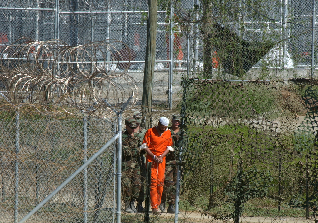 FILE - In this March 1, 2002 file photo, a detainee is escorted to interrogation by U.S. military guards in the temporary detention facility Camp X-Ray at the Guantanamo Bay U.S. Naval Base in Cuba. Open for 10 years on Wednesday Jan. 11, 2012, the Guantanamo Bay prison seems more established than ever. The deadline set by President Barack Obama to close it came and went two years ago. No detainee has left in a year because of restrictions on transfers, and indefinite military detention is now enshrined in U.S. law. Prisoners at the U.S. base in Cuba plan to mark the day with sit-ins, banners and a refusal of meals, said Ramzi Kassem, a lawyer who represents seven inmates. (AP Photo/Andres Leighton, File) === MARCH 1, 2002 FILE PHOTO === 