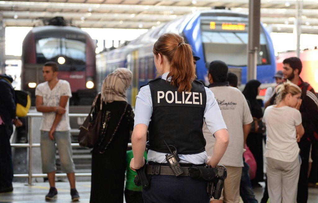epa04906567 A policewoman stands in front of Syrian refugees, who wait for their registration and ID documents, at the central train station in Munich, Germany, 31 August 2015. Between 50 and 60 refugees arrived on a train from Hungary via Austria. EU interior ministers are to hold emergency talks on 14 September 2015 aimed at improving the bloc's response to the current migration crisis, the European Union's rotating presidency announced. Europe is grappling with the biggest flow of migrants since World War II. Many of them are fleeing war-torn countries such as Syria and Afghanistan, risking their lives in perilous journeys to reach affluent Western states.  EPA/ANDEAS GEBERT