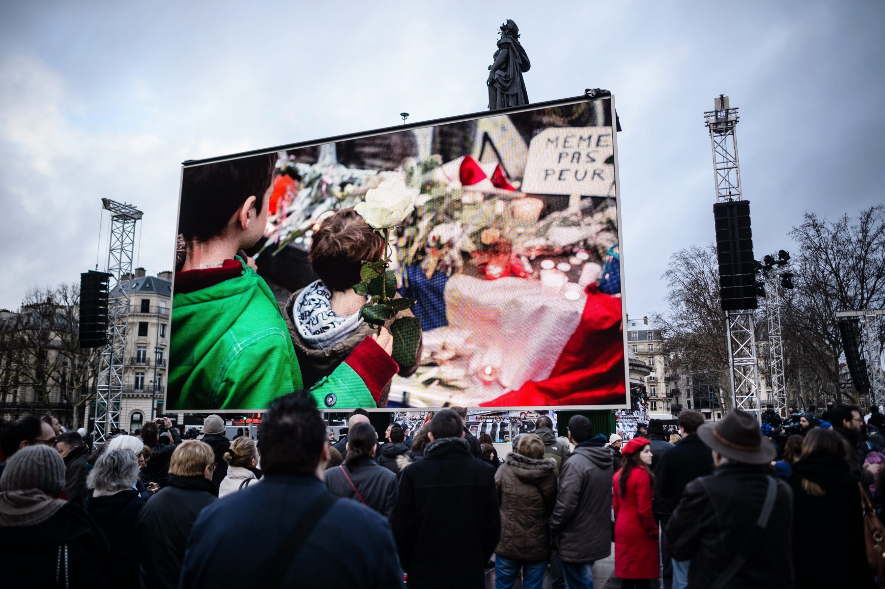 epa05095285 The gathered people watch a slide show on a screen at a ceremony to honor the victims of the terrorist attacks in 2015, at the Republic Square in Paris, France, 10 January 2016. France this week commemorates the victims of last year's Islamist militant attacks on satirical weekly Charlie Hebdo and a Jewish HyperCacher supermarket.  EPA/CHRISTOPHE PETIT TESSON FRANCE ATTACKS ANNIVERSARY