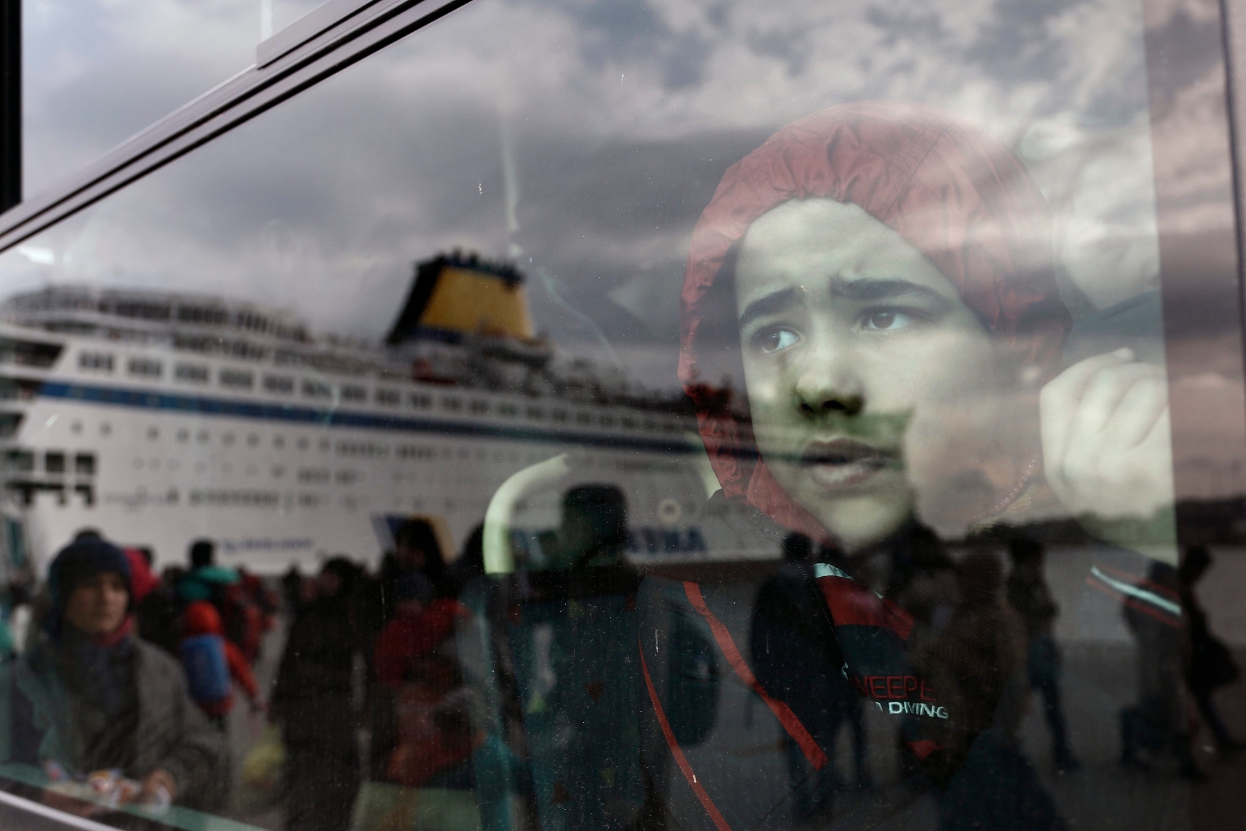 epa05120127 A refugee boy looks on inside a bus as the ferry 'Eleftherios Venizelos is reflected on it, after its arrival at the port of Piraeus, near Athens, Greece, 23 January 2016. The ship 'Eleftherios Venizelos' arrived at the port of Piraeus carrying about 2,500 refugees and migrants that had landed on the Greek island of Myilene, coming from Turkey. Thousands of migrants continue to arrive on the Greek islands, after having crossed the Aegean sea, on their way to the European Union countries.  EPA/YANNIS KOLESIDIS GREECE REFUGEES MIGRANTS SITUATION