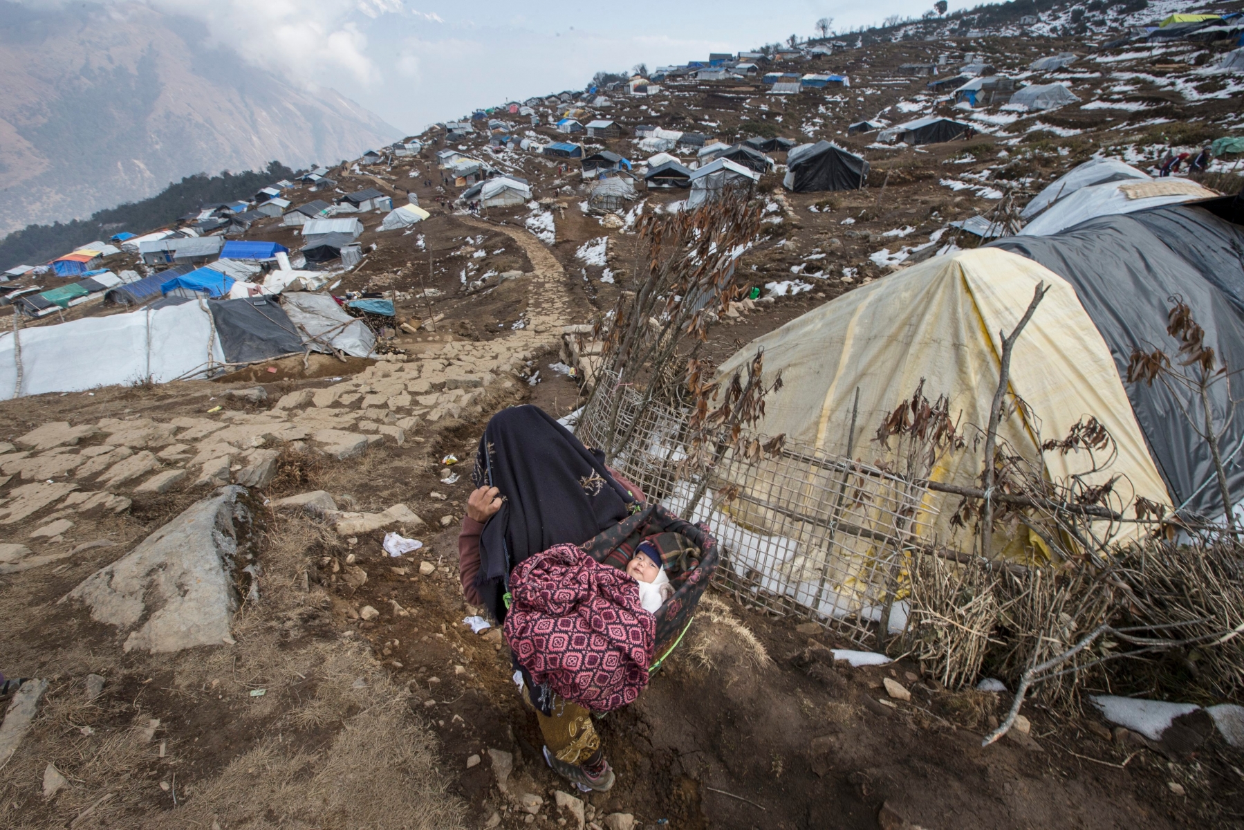 epa05247234 (02/45) A mother carries her son on a basket after a snowfall outside the shelter for earthquake victims in Gupsipakha, Laprak, Gorkha district, Nepal, 17 January 2016. Laprak was one of the epicenter villages of the April 2015 earthquake where more than 600 hundred houses were destroyed. Millions of Nepalese are still struggling with the harsh reality of 25 April 2015 when a 7.9-magnitude earthquake struck the nation. It killed more than 9,000 people, injured at least 23,000, wiped out 200,000 homes, 20,000 schools and destroyed more than 700 monuments.  EPA/NARENDRA SHRESTHA PLEASE REFER TO ADVISORY NOTICE (epa05247232) FOR FULL FEATURE TEXT NEPAL FEATURE PACKAGE REBUILDING AFTER EARTHQUAKE