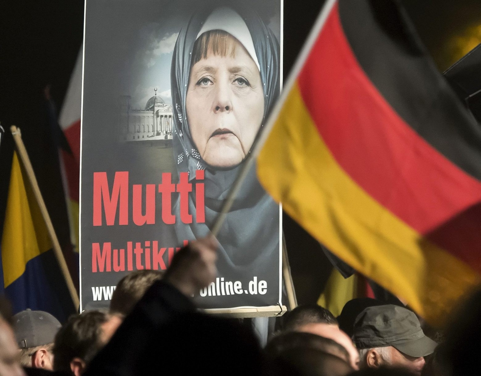 A banner reading 'Mum multiculti' and depicting a manipulated image German Chancellor Angela Merkel is carried by a protester behind the German flag as some thousands of people take part in a demonstration initiated by the Alternative for Germany (AfD) party against what they call the uncontrolled immigration and asylum abuse in Erfurt, central Germany, Wednesday, Oct. 28, 2015. (AP Photo/Jens Meyer) Germany Protests