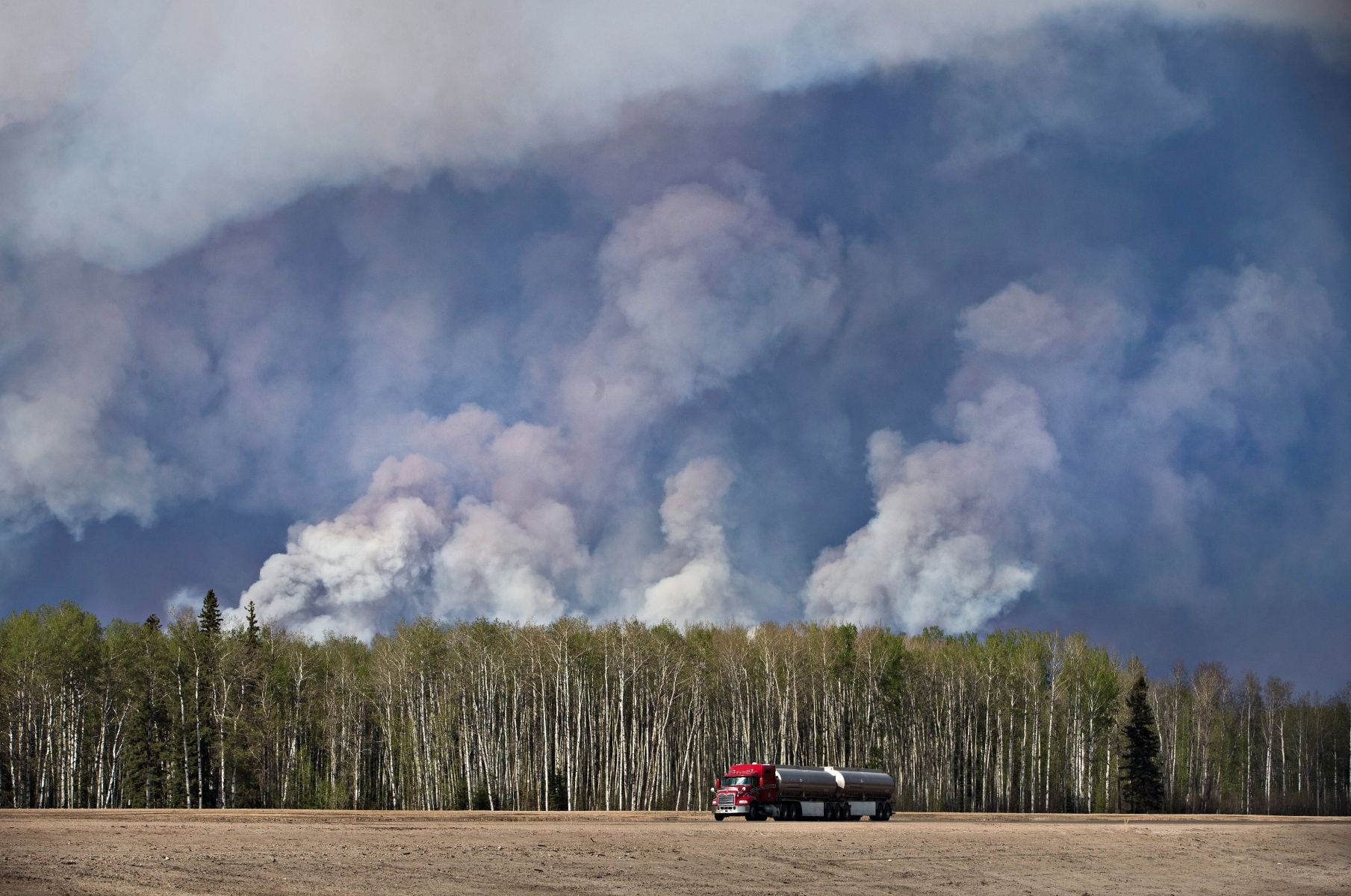 A semi truck drives away from a wildfire in Fort McMurray, Canada, Thursday, May 5, 2016. The massive wildfire raging in the Canadian province of Alberta grew to 85,000 hectares (210,035 acres) and officials said Thursday they would like to move south about 25,000 evacuees who had previously fled north, including 8,000 by air. (Jason Franson/The Canadian Press via AP) MANDATORY CREDIT Canada Wildfire