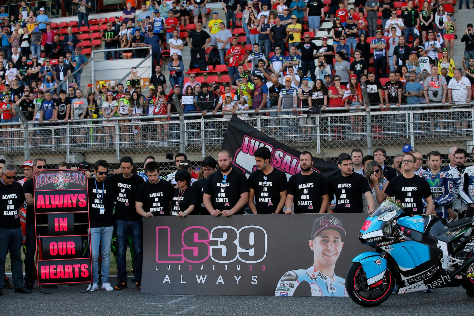 Riders, mechanics and staff gather around the motorcycle and a photo of Moto 2 rider Luis Salom during a minute of silence in his memory before the Catalunya Motorcycle Grand Prix at the Barcelona Catalunya racetrack in Montmelo, just outside Barcelona, Spain, Sunday, June 5, 2016. Salom died in a crash during Friday's free practice for the Grand Prix. (AP Photo/Manu Fernandez) Spain Motorcycle Grand Prix