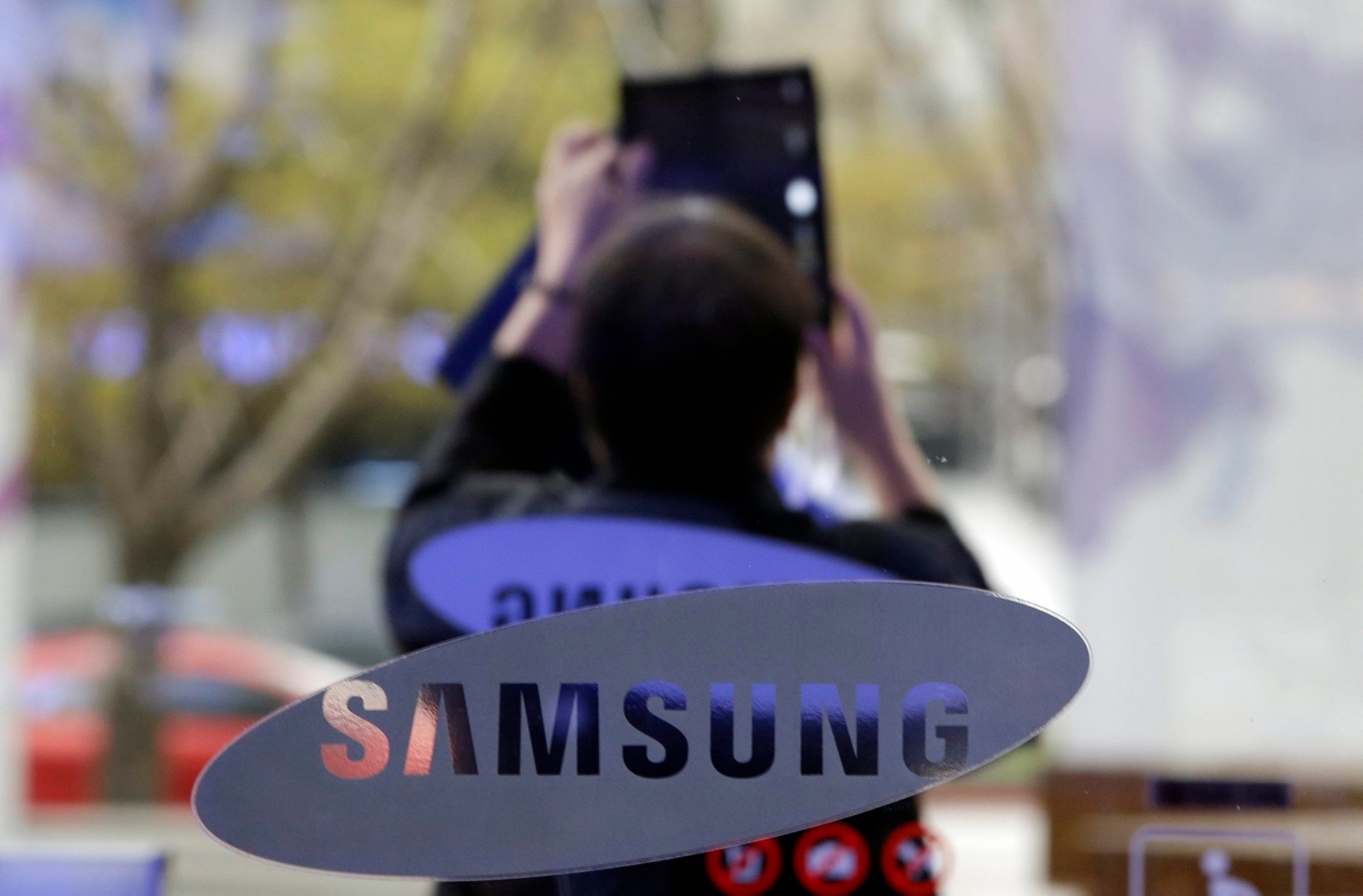 A visitor takes a picture near the logo of Samsung Electronics Co. outside its showroom in Seoul, South Korea, Tuesday, April 7, 2015. Samsung's quarterly operating earnings fell 31 percent from a year earlier but the drop wasn't as big as expected in a sign the smartphone and computer chip giant may be emerging from its profit slump. (AP Photo/Lee Jin-man) South Korea Earns Samsung Electronics