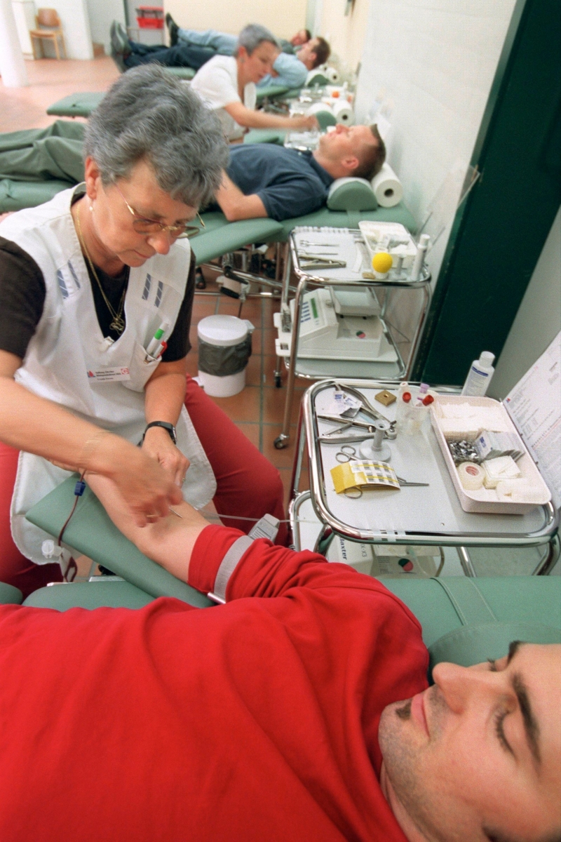 THEMENBILD --- Eine Mitarbeiterin des Blutspendedienstes Zuerich hilft einem freiwilligen Spender beim Blutspenden am 2. Juli 2003 im Limmattal-Spitale in Schlieren. Offenbar wegen der Fussball-WM und des heissen Sommerwetters gehen weit weniger Leute als sonst Blut spenden. Damit es nicht zu einem Notstand kommt, hat der Blutspendedienst des Schweizerischen Roten Kreuzes (SRK) die Bevoelkerung am 26. Juni 2006 zur Blutspende aufgerufen. Die Blutspenden sind in den letzten zwei Wochen um durchschnittlich 30 Prozent zurueckgegangen. Gleichzeitig stieg der Bedarf an Blutprodukten im Juni massiv an. In zahlreichen Spitaelern fanden Operationen mit besonders hohem Blutbedarf statt. Dies fuehrt laut dem Blutspendedienst SRK dazu, dass jetzt, kurz vor den Sommerferien, die Blutreserven bedenklich knapp geworden sind. Da in den Sommerferien erfahrungsgemaess ohnehin deutlich weniger Personen Blut spenden, koennte dies im August zu Engpaessen fuehren. Der Blutspendedienst SRK ruft deshalb die