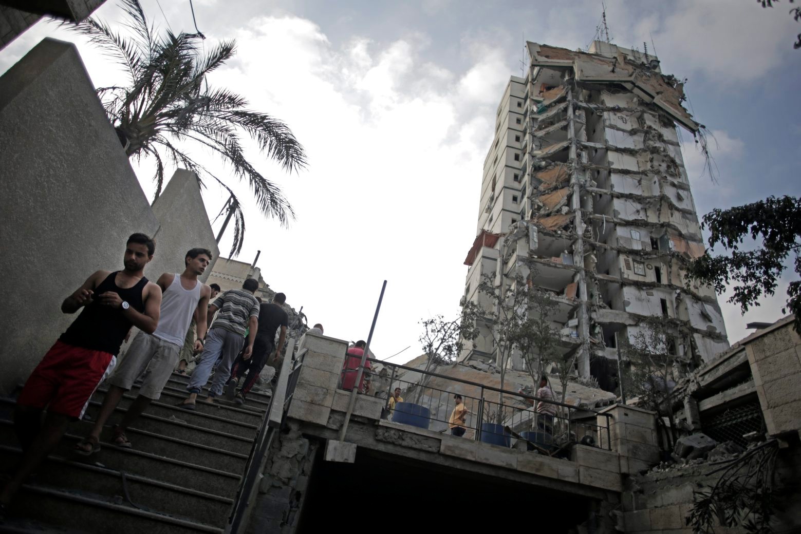 Palestinians walk near the damaged Italian Complex high-rise following several late night Israeli airstrikes in Gaza City, Tuesday, Aug. 26, 2014. Israel bombed two Gaza City high-rises with dozens of homes and shops Tuesday, collapsing the 15-story Basha Tower and severely damaging the Italian Complex in a further escalation in seven weeks of cross-border fighting with Hamas. (AP Photo/Khalil Hamra) Mideast Israel Palestinians