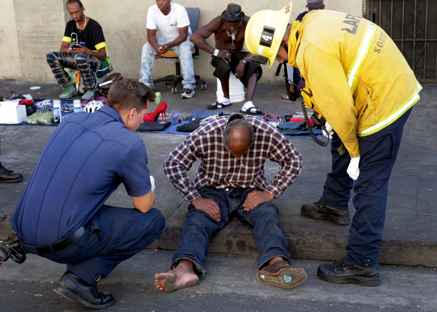Los Angeles paramedics and firefighters evaluate a person who fell ill in the Skid Row section of Los Angeles, Friday, Aug. 19, 2016. Fire Department officials say paramedics responded to the area on Friday afternoon and took over a dozen people to hospitals from the downtown area where the homeless gather. Officials have not yet determined what may have caused the sicknesses. (AP Photo/Nick Ut) APTOPIX Homeless Illnesses