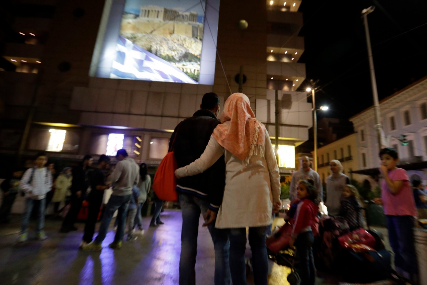 Refugees wait under an advertising banner, depicting Acropolis and the Greek flag, at Omonia square in Athens before heading to the airport for a flight to Madrid on Monday, Sept. 26, 2016. A group of 27 Syrians and four Iraqis was among the very few accepted by a European country as part of a sputtering relocation program designed to relieve pressure on Greece and Italy, the main entry points for those fleeing war and hoping for better lives in the European Union. (AP Photo/Thanassis Stavrakis) EUROPE MIGRANTS FAMILY'S ODYSSEY