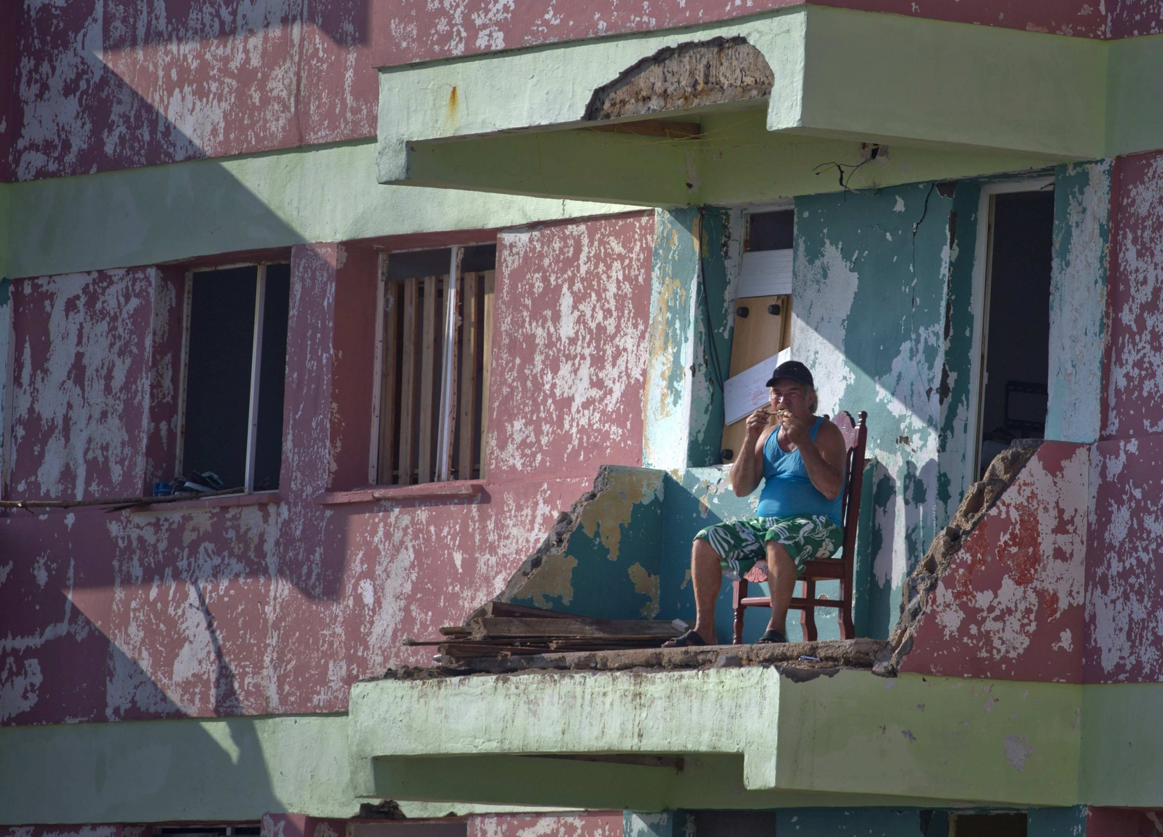 A man eats a piece of chicken while sitting on his balcony that was damaged by Hurricane Matthew, in Baracoa, Cuba, Friday, Oct. 7, 2016. Matthew hit Cuba's lightly populated eastern tip Tuesday night, damaging hundreds of homes in the easternmost city of Baracoa but there were no reports of deaths. Nearly 380,000 people were evacuated and measures were taken to protect infrastructure. (AP Photo/Ramon Espinosa) APTOPIX Cuba Hurricane Matthew