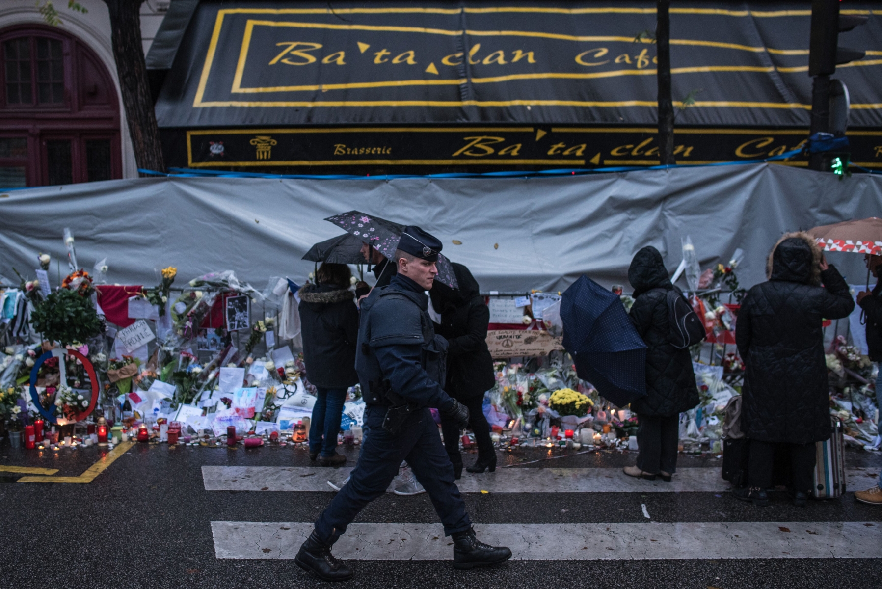 A policeman walks as people pay respects to victims of the Paris attacks in front of the Bataclan concert hall, Wednesday, Nov. 25, 2015, in Paris. Authorities in France and Belgium have issued public appeals for help in tracking down two men believed directly linked to the Paris attacks that killed 130 people and wounded hundreds in shootings and suicide bombings in the French capital. (AP Photo/Kamil Zihnioglu) FRANKREICH TERRORISMUS ANSCHLAEGE PARIS