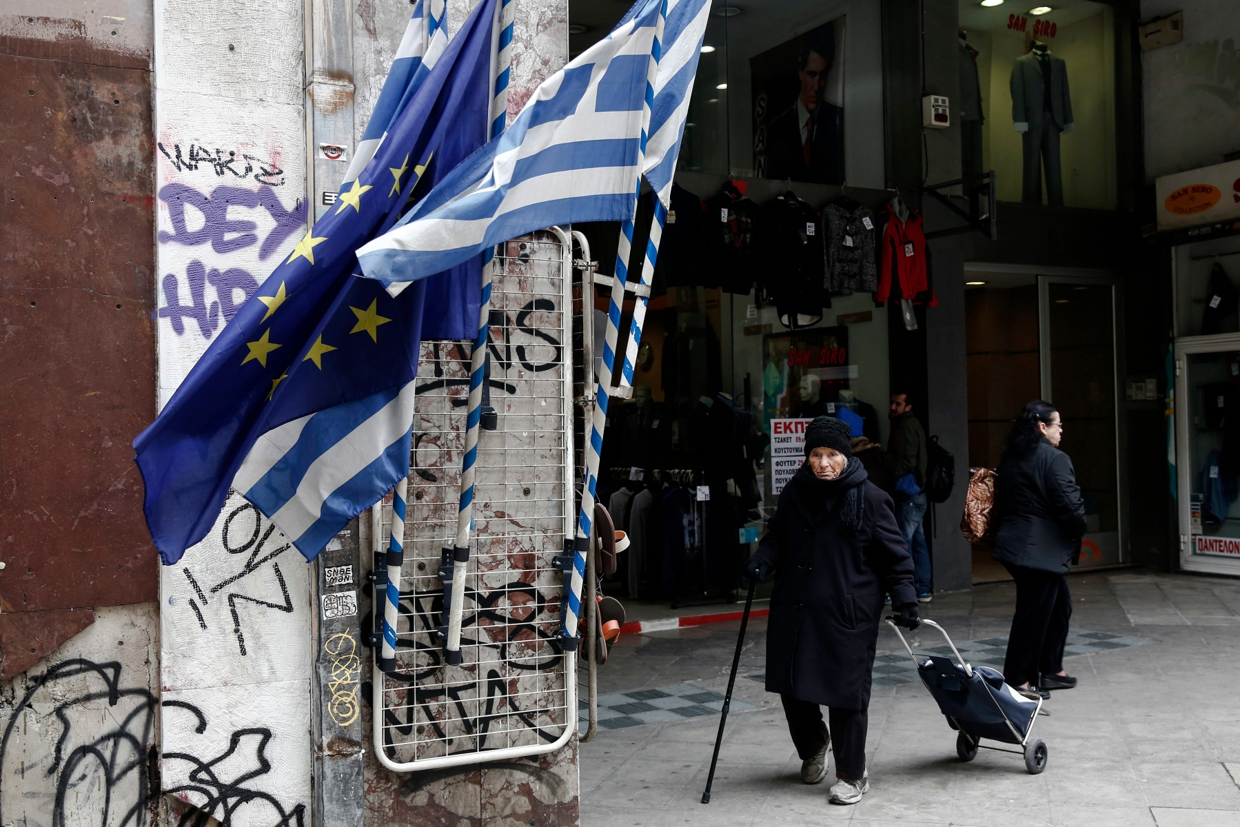 A woman pulls a shopping trolley next to a Greek and an EU flags at a main street of Athens, Thursday, Jan. 26, 2017. Greece's prime minister on Wednesday marked two years in office, as talks with bailout lenders remain at an impasse. (AP Photo/Yorgos Karahalis) Greece Bailout