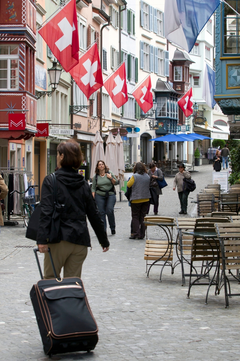 Eine Frau zieht ihren Koffer durch die Augustinergasse, die mit Schweizerfahnen geschmueckt ist am Dienstag, 9. August 2011 in Zuerich. (KEYSTONE/Alessandro Della Bella) SCHWEIZ TOURISMUS