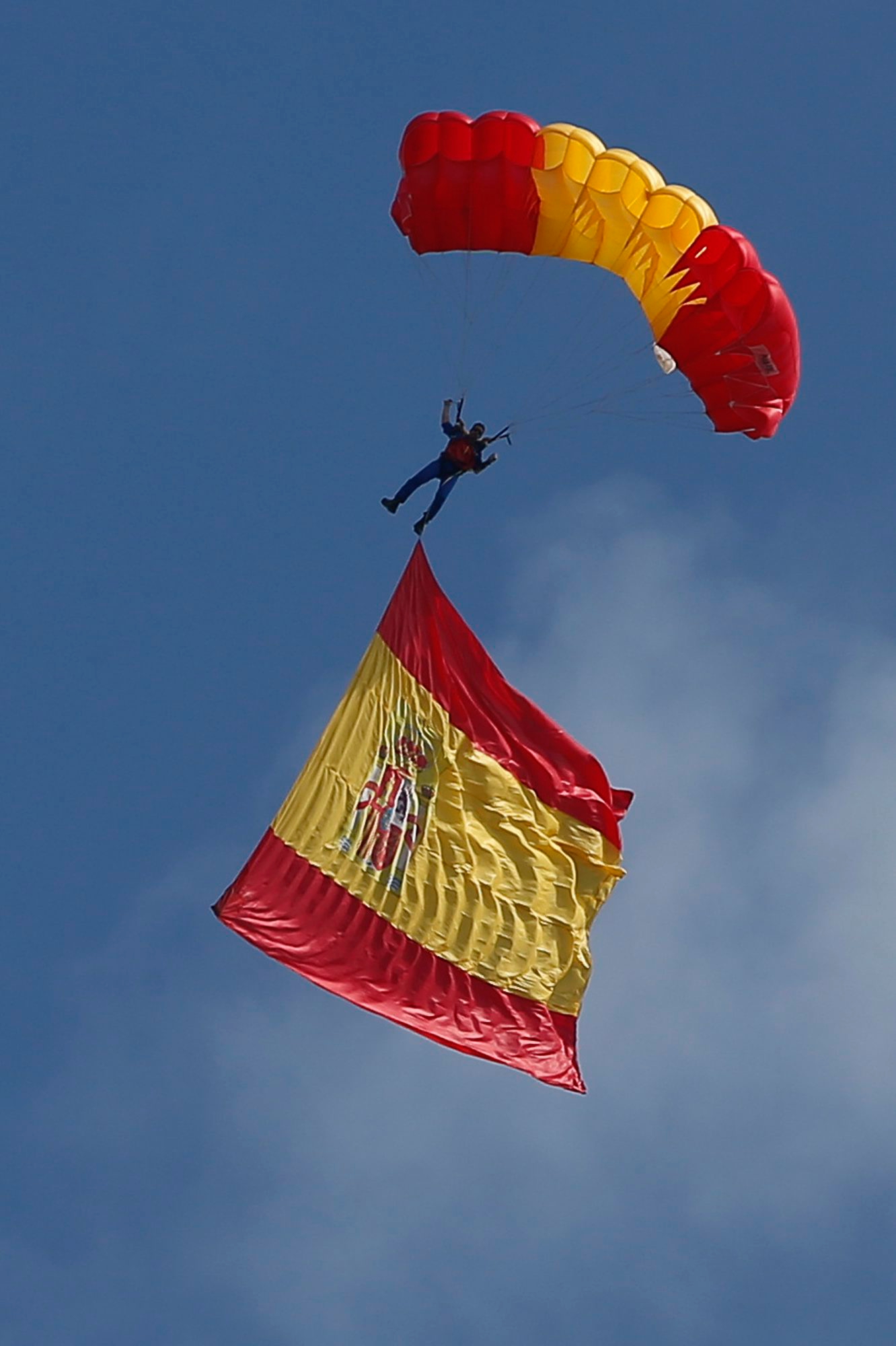 A parachutist with a large Spanish flag floats down during a military parade on the national holiday known as "Dia de la Hispanidad" or Hispanic Day, in Madrid, Spain, Thursday, Oct. 12, 2017. King Felipe VI presided over the annual colorful parade Thursday as Spain awaits a response to a government request to Catalonia to clarify by Monday if it has already declared independence, in which case Spain warns it may begin taking control of the region. (AP Photo/Paul White) Spain Catalonia