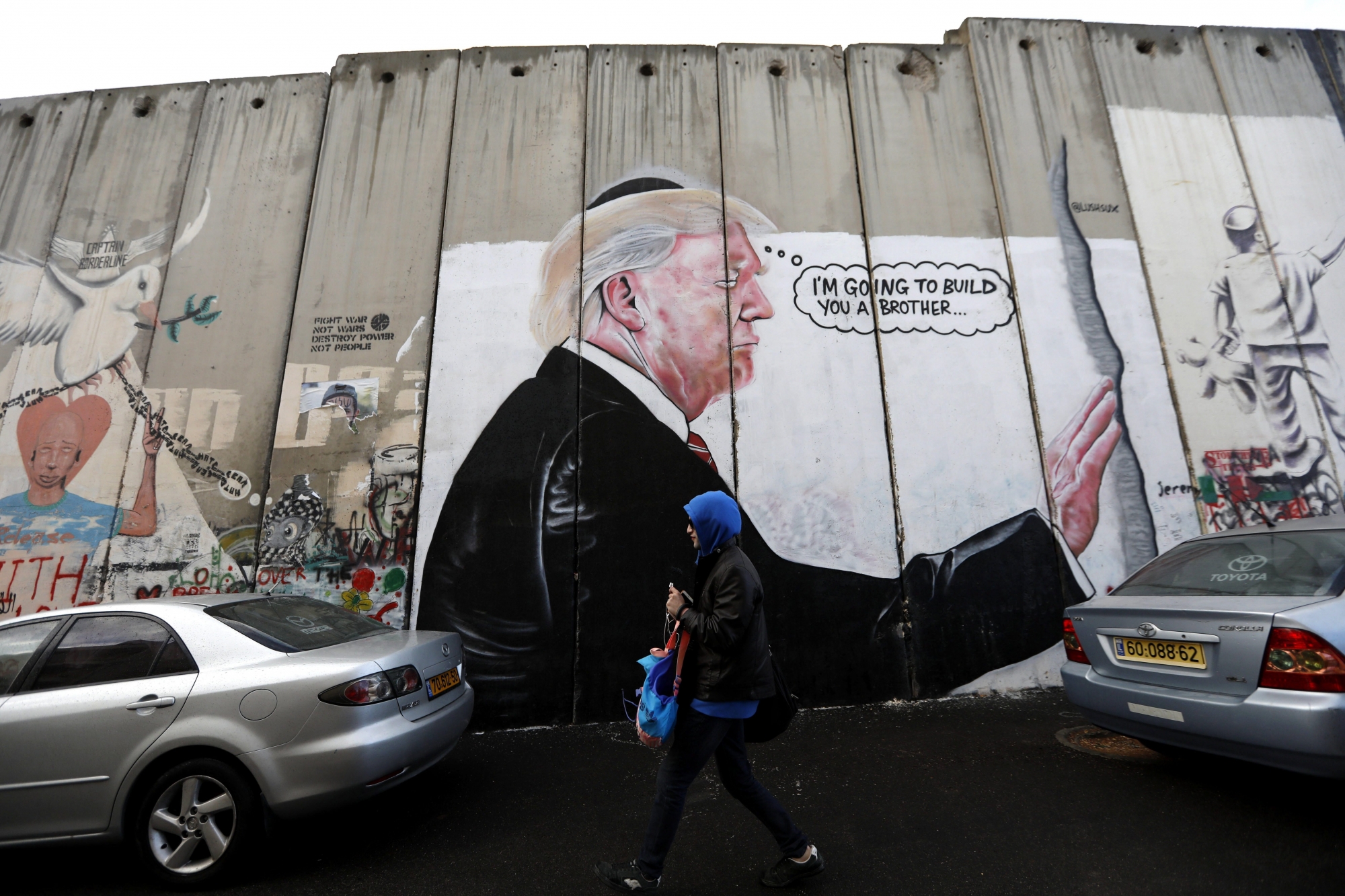 epa06371378 A woman walks in front of a sprayed graffiti of US President Donald Trump is seen on the Israeli separation wall in the West Bank city of Bethlehem, 06 December 2017. According to media reports, US President Donald J. Trump has informed Palestinian leader Mahmoud Abbas that he intends to recognize Jerusalem as the Israeli capital and will relocate the US embassy from Tel Aviv to Jerusalem.  EPA/ABED AL HASHLAMOUN MIDEAST PALESTINIANS ISRAEL USA DIPLOMACY JERUSALEM