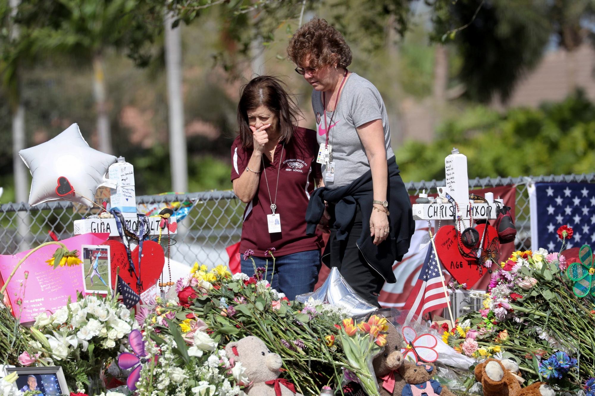 Margarita Lasalle, a bookkeeper and Joellen Berman, a guidance data specialist, look at a memorial Friday, Feb. 23, 2018 as teachers and school administrators returned to Marjory Stoneman Douglas High School for the first time since 17 victims were killed in a mass shooting at the school, in Parkland, Fla. (Mike Stocker/South Florida Sun-Sentinel via AP) School Shooting Florida