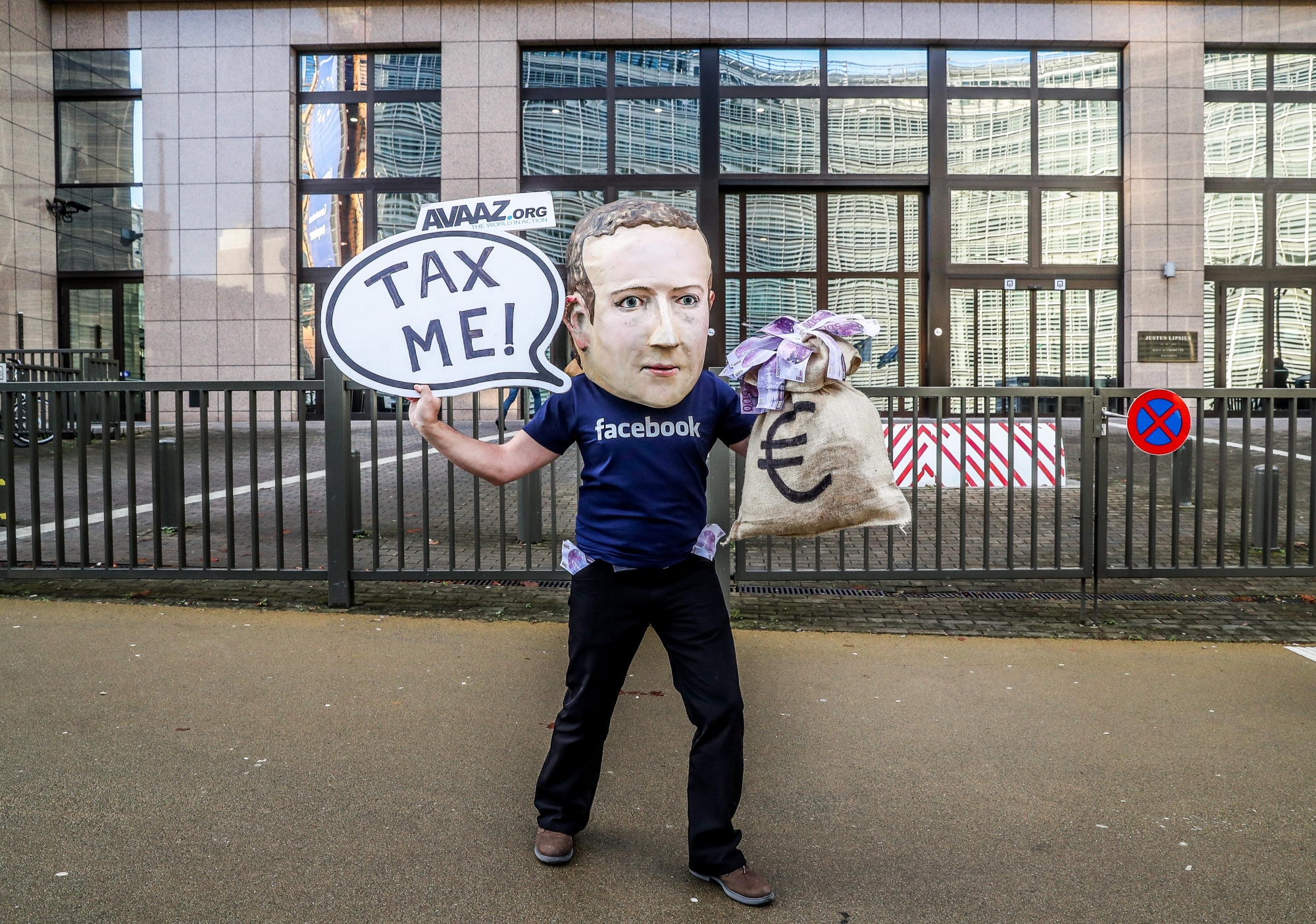 epa07207690 An activist wearing a mask depicting Facebook's CEO Mark Zuckerberg holds a banner reading 'Tax me' at the start of an European Union Finance Ministers Meeting in front of the European Council in Brussels, Belgium, 04 December 2018. Activists ask for an EU tax on big digital firms.  EPA/STEPHANIE LECOCQ BELGIUM EU DIGITAL TAX