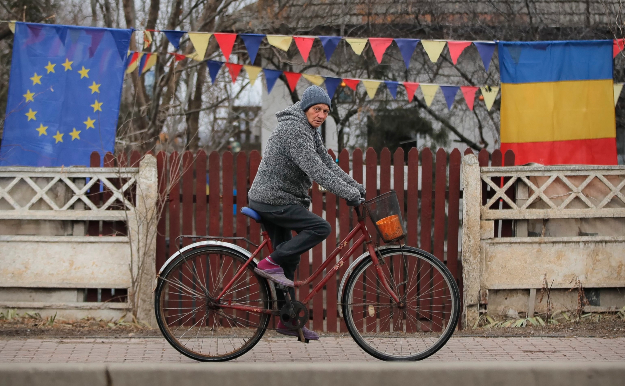 In this Sunday, Dec. 30, 2018, photo a person rides a bicycle by a yard decorated with European Union and Romanian flags in Tartasesti, Romania, two days before the country will take over the EU's rotating presidency. Romanian officials have slammed European Union officials for treating it as "a second-rate" country as it prepares to take over the EU's rotating presidency. (AP Photo/Vadim Ghirda) Romania EU Presidency