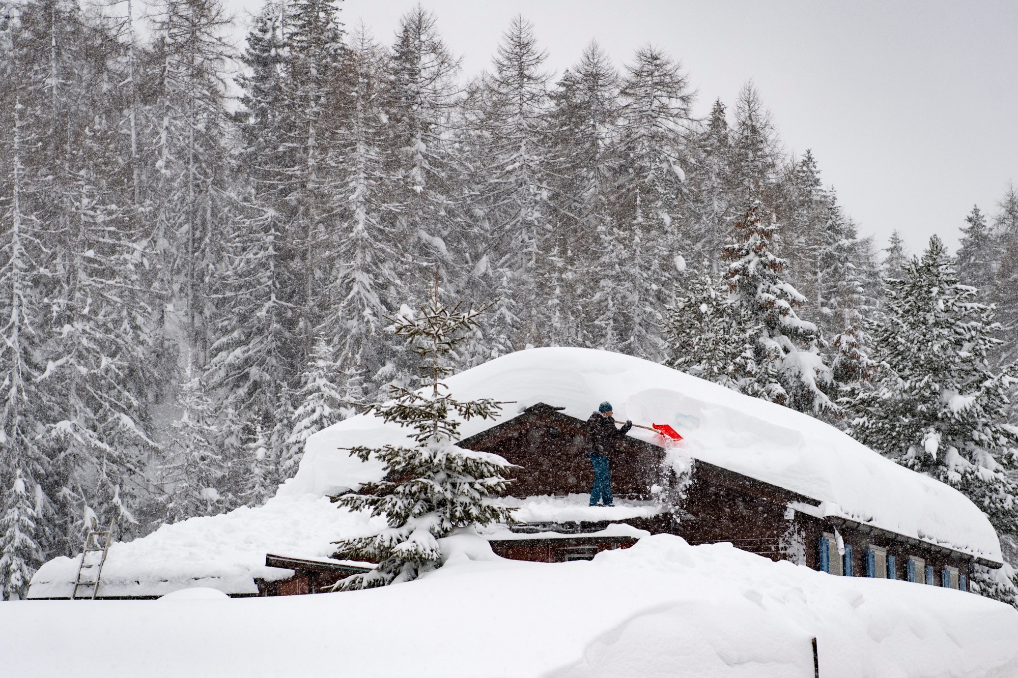 A man clears the roof of his house of snow, in Davos Laret, on Monday, January 14, 2019. Switzerland faces big amounts of snowfall. The danger for avalanches in large parts of the alps has risen to the highest.(KEYSTONE/Gian Ehrenzeller) SWITZERLAND WINTER SNOW