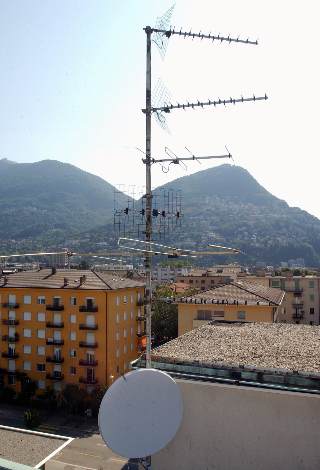 Eine herkoemmliche TV Empfangsantenne, oben, und eine Parabolantenne (Satellitenschuessel) auf einem Hausdach in Lugano, aufgenommen am Montag, 24. Juli 2006. Im Tessin hat heute das digitale TV-Zeitalter begonnen. Die Suedschweiz ist die erste Region, in der die SRG die analoge terrestrische Verbreitung ihrer Programme abgeschaltet hat. Rund 25 000 TV-Apparate waren von der Umstellung betroffen. 
 (KEYSTONE/Karl Mathis) SCHWEIZ FERNSEHEN EMPFANG ANTENNE