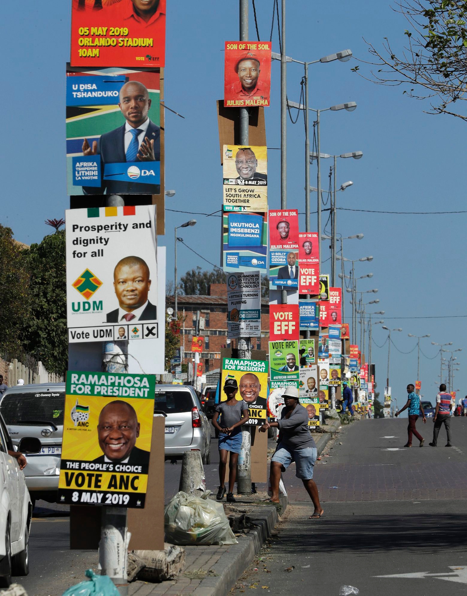 In this May 1, 2019, photo, people walk down a main street in Alexandra township, adorned with election posters. Twenty-five years after the end of apartheid, inequality is still on display in South Africa. The frustration could play out as the country holds a national election on Wednesday, May 8, 2019. (AP Photo/Themba Hadebe) South Africa Election Gaping Inequality