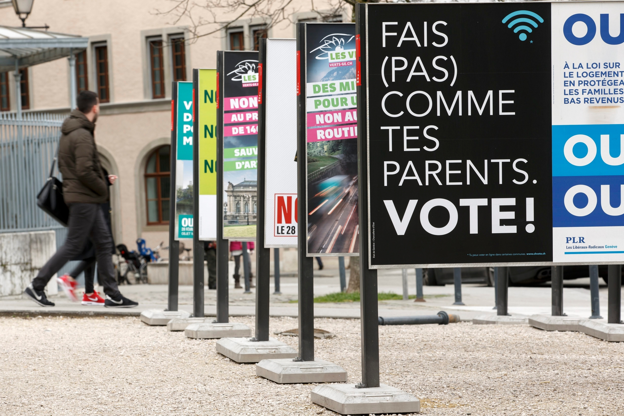 Des personnes passent vers l'affiche "Fais (pas) comme des parents. Vote!" du Conseil d'Etat genevois, et d'autres affiches concernant les votations du 28 fevrier, ce mercredi 24 fevrier 2016 a Geneve. Le Conseil d'Etat genevois a fait placarder des affiches pour incite les jeunes a voter. (KEYSTONE/Salvatore Di Nolfi) SUISSE AFFICHE VOTATION GE