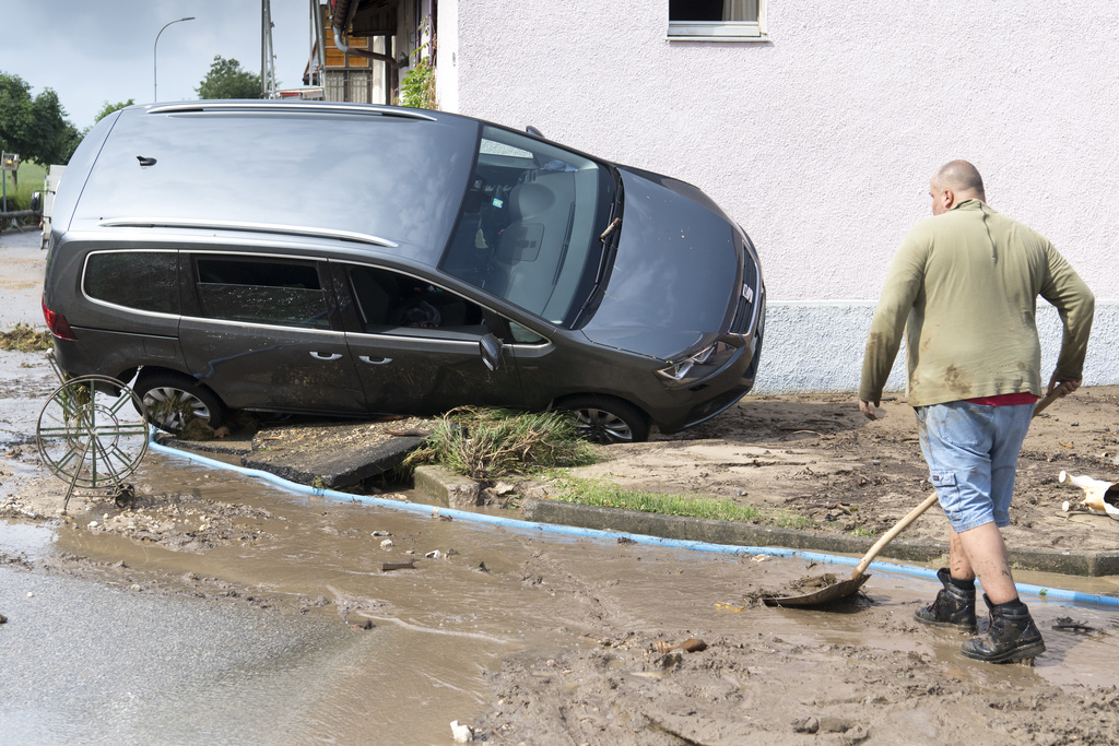 Un homme nettoie la boue devant une carcasse de voiture emportée lors du violent orage de vendredi à Dombresson.