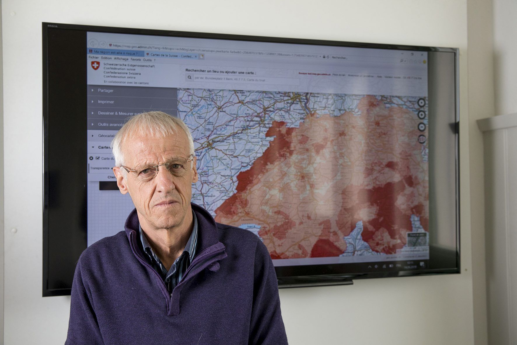 Pierre Renaud, ingénieur-conseils en énergie et environnement au bureau Planair de La Sagne, devant une carte de la Suisse, où les régions les plus touchées par le radon sont en rouge vif.