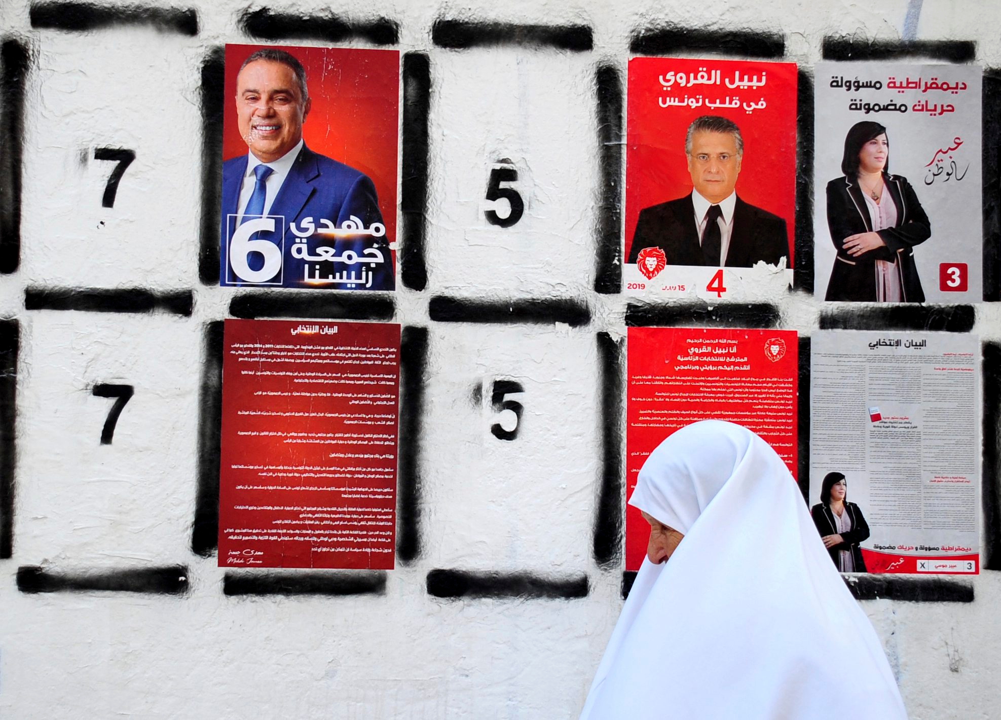 FILE - In this Sept. 4, 2019 file photo, a woman walks past a wall of campaign posters in Tunis. Twenty-six candidates are running for president of Tunisia in a cacophonous election seen as key to securing the country's young democracy. The first-round presidential vote is being held Sunday Sept. 15, 2019. (AP Photo/Hassene Dridi, File) TUNISIA PRESIDENTIAL ELECTION