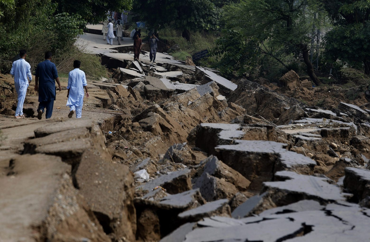 Residents walk alongside a damaged portion of a road caused by a powerful earthquake in Jatlan near Mirpur, in northeast Pakistan, Wednesday, Sept. 25, 2019. Thousands of people whose homes were damaged because of a strong earthquake are desperately waiting for the arrival of government help, 22 hours after the 5.8 magnitude tremor struck Pakistan-held Kashmir and elsewhere, killing 25 people and injuring 700. (AP Photo/Anjum Naveed) APTOPIX Pakistan Earthquake