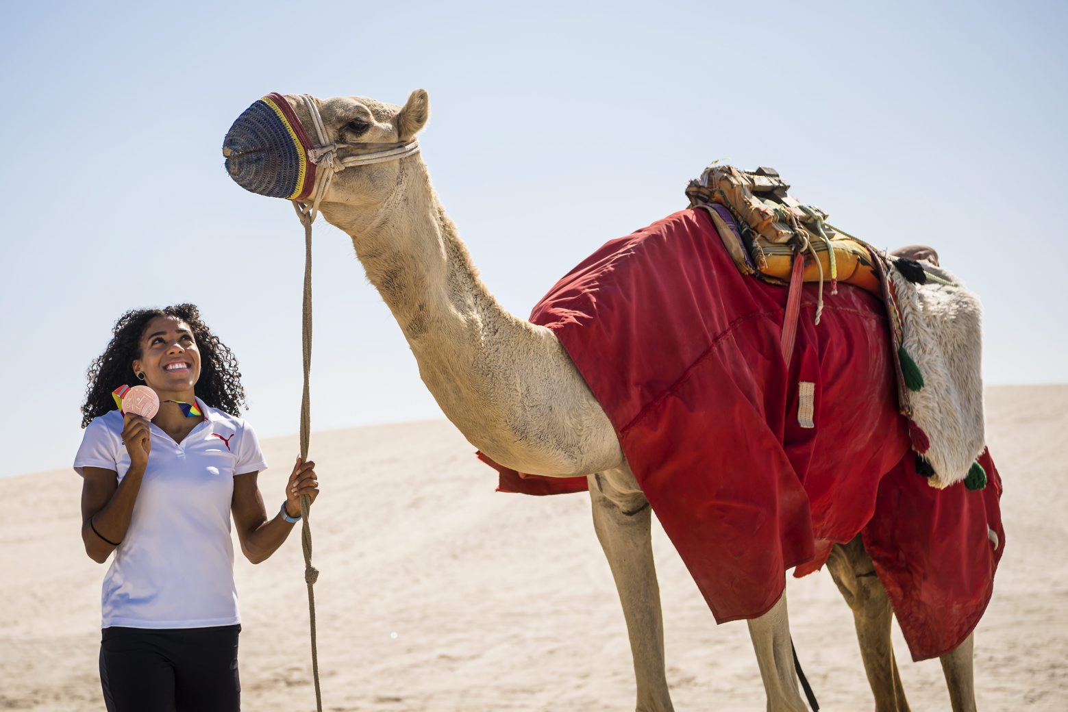 Mujinga Kambundji from Switzerland poses with a camel and the bronze medal of the women's 200 meters race during the IAAF World Athletics Championships, in the sand dunes near Doha, Qatar, Sunday, October 6, 2019. (KEYSTONE/Jean-Christophe Bott) QATAR WORLD ATHLETICS CHAMPIONSHIPS