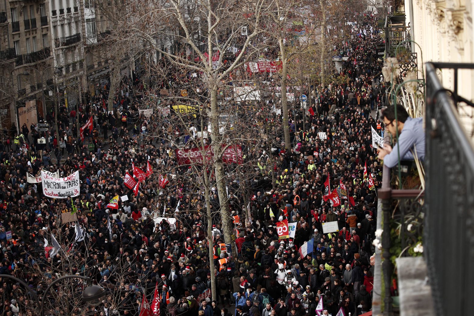epa08077066 A man looks at the crowd from a balcony as thousands of protesters participate in a demonstration against pension reforms near Republique Square in Paris, France, 17 December 2019. Unions representing railway and transport workers and many others in the public sector have called for a general strike and demonstration to protest against French government's reform of the pension system.  EPA/YOAN VALAT FRANCE GENERAL STRIKE
