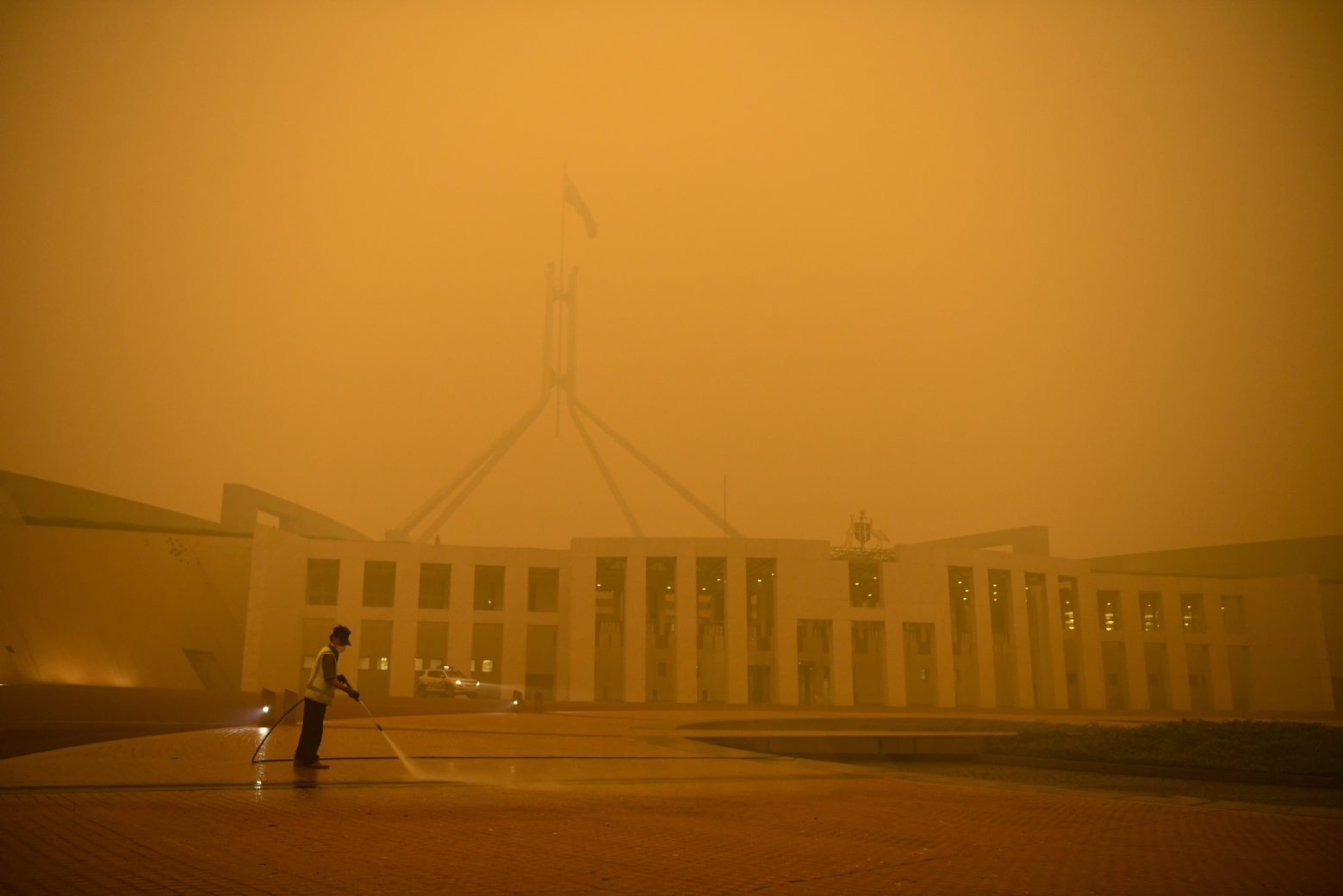 epa08103061 A man cleans the forecourt of Parliament House surrounded by smoke haze early morning in Canberra, Australia, 05 January 2020.  EPA/LUKAS COCH AUSTRALIA AND NEW ZEALAND OUT AUSTRALIA CANBERRA SMOKE HAZE
