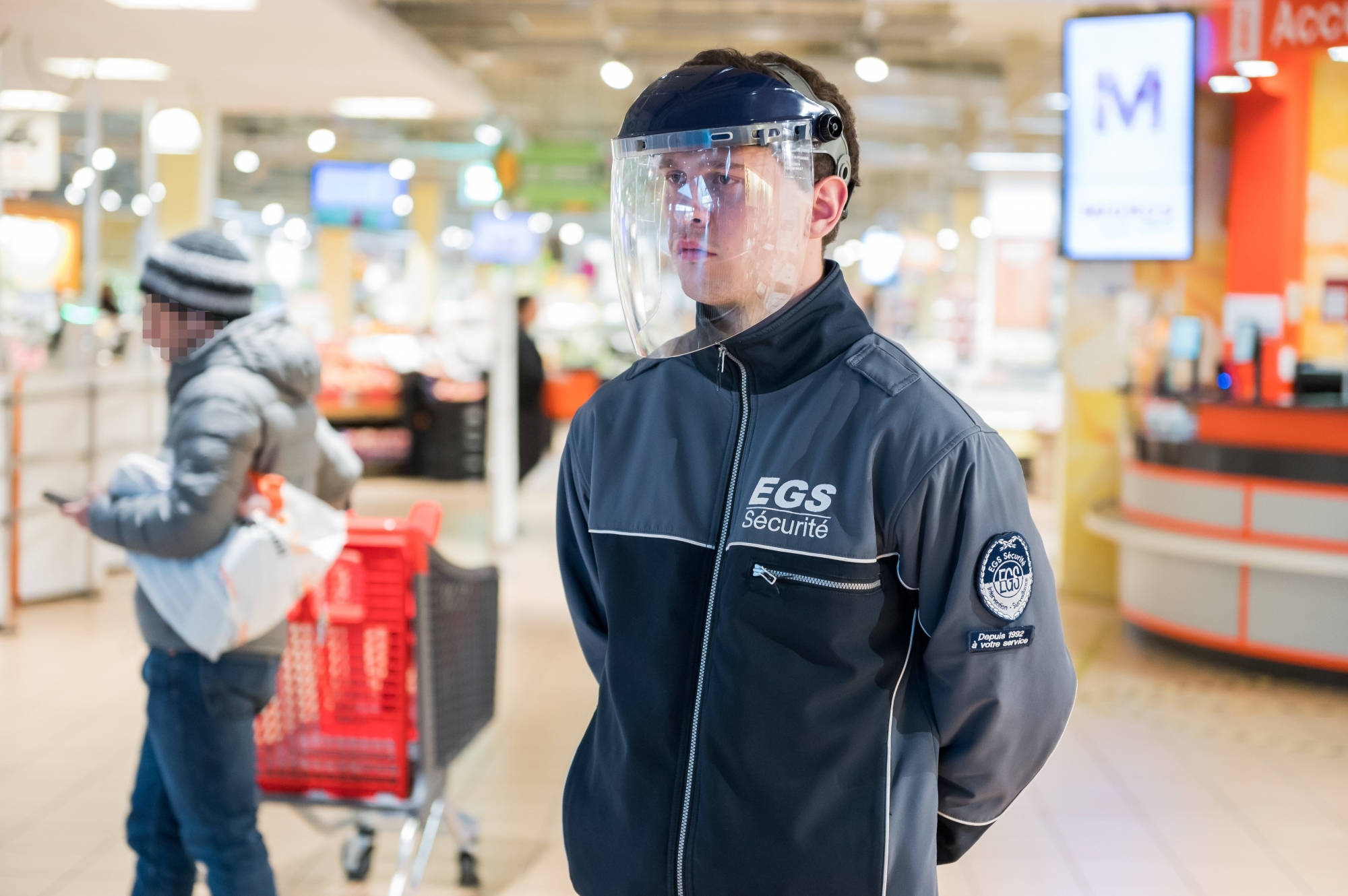 Pour contrôler le flux des clients, certains magasins d'alimentation recourent à des agents de sécurité. Ceux-ci se protègent aussi contre le nouveau coronavirus.