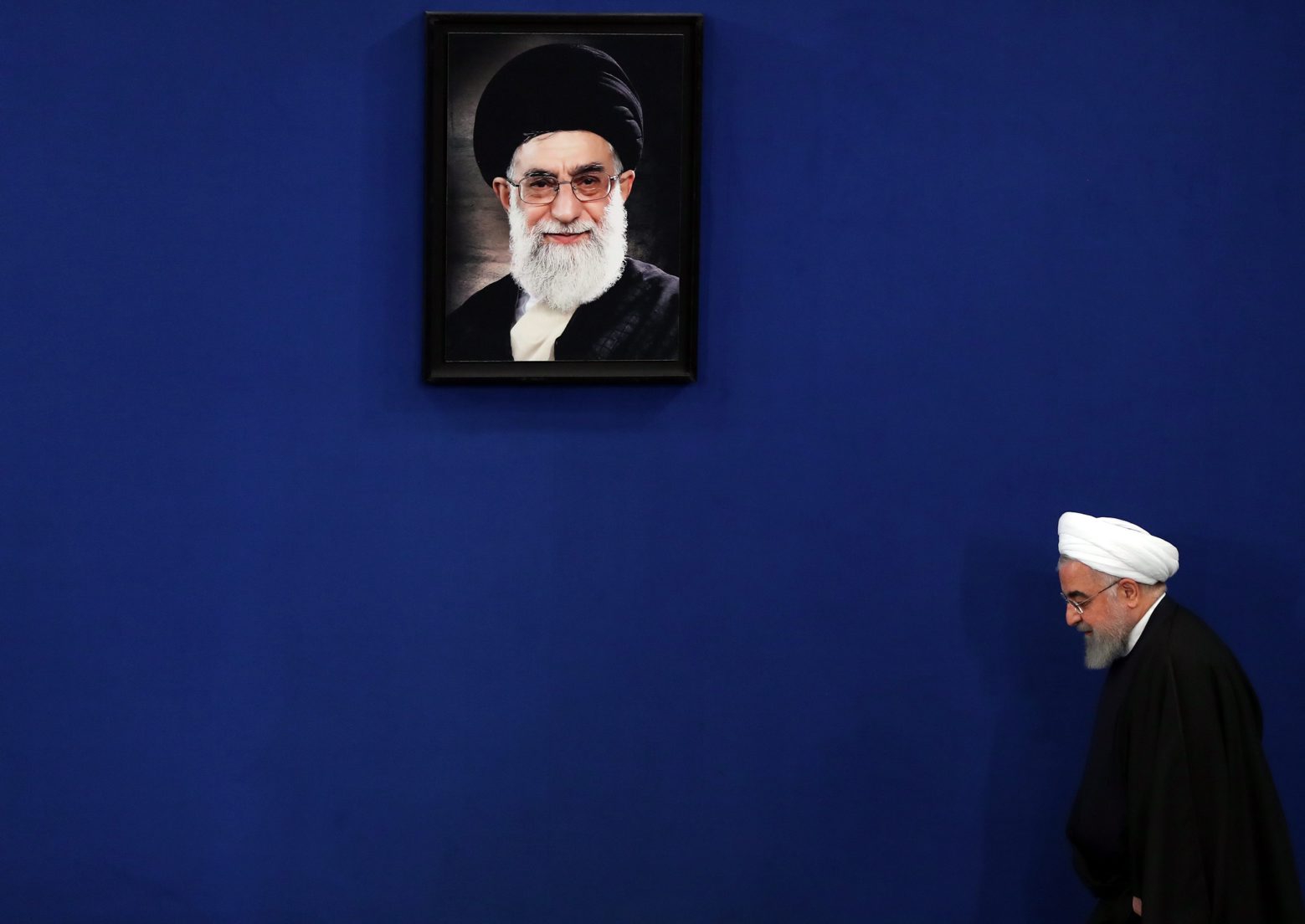 epa08222022 Iranian President Hassan Rouhani walks next to a picture of Iranian supreme leader Ayatollah Ali Khamenei, upon arrival for a press conference in Tehran, Iran, 16 February 2020.  EPA/ABEDIN TAHERKENAREH IRAN ROUHANI PRESS CONFERENCE
