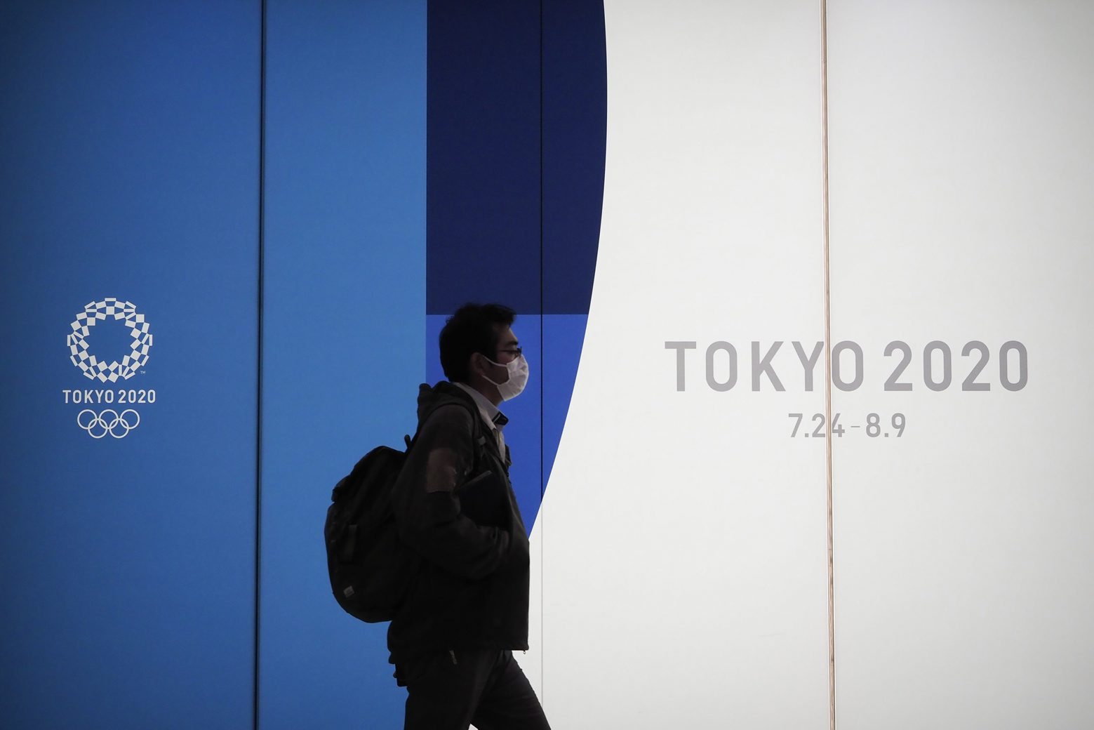 A man walks past a large display promoting the Tokyo 2020 Olympics in Tokyo, Friday, March 13, 2020. U.S. President Donald Trump's suggestion to postpone the Tokyo Olympics for a year because of the spreading coronavirus was immediately shot down by Japan's Olympic minister. For most people, the new coronavirus causes only mild or moderate symptoms. For some it can cause more severe illness. (AP Photo/Jae C. Hong) Virus Outbreak Japan