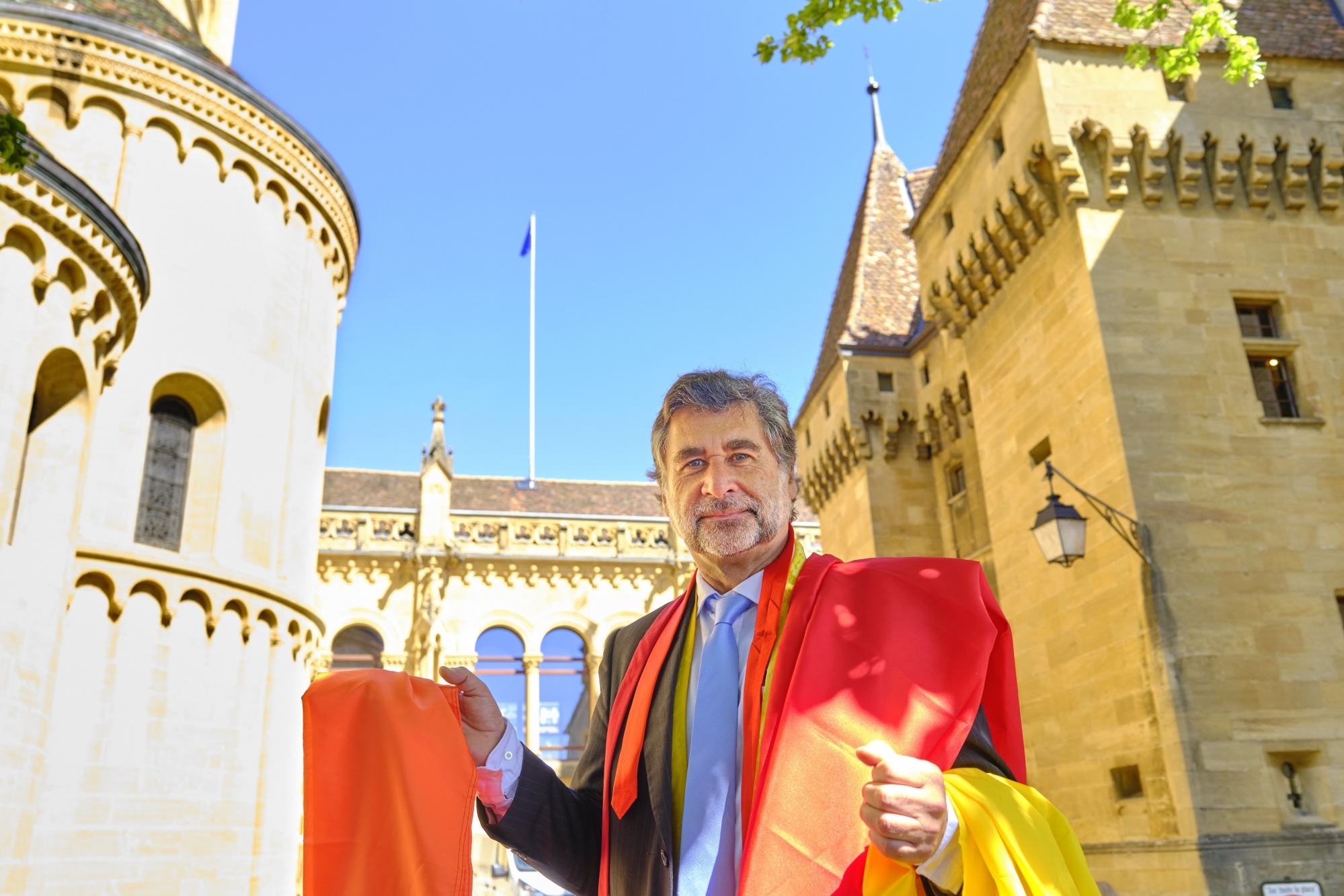Le médecin cantonal Claude-François Robert avec les drapeaux et ses cravates devant le château où flotte le drapeau bleu.
