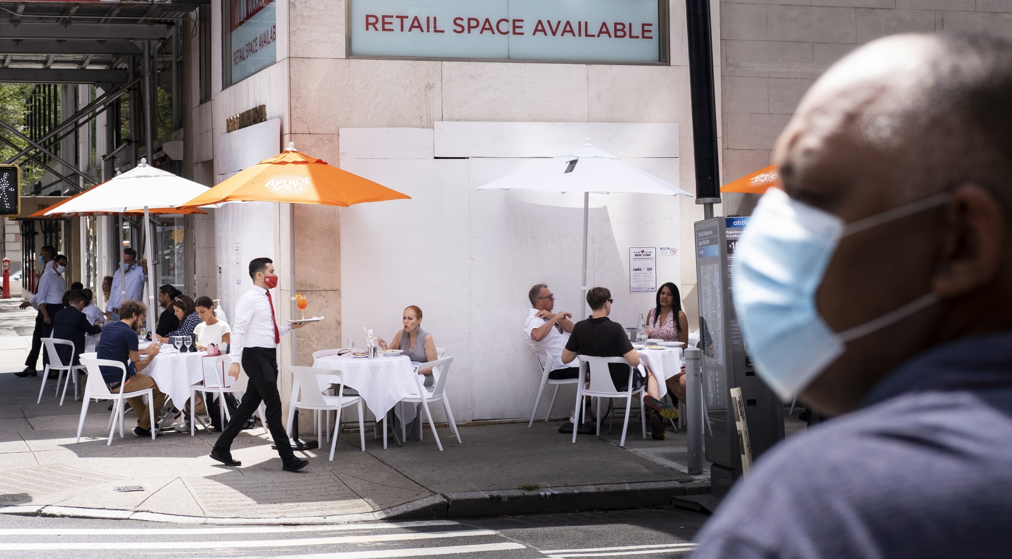 epa08627643 People sit at a restaurant's sidewalk table, set up because indoor dining is still not permitted in the city, in front of a closed designer store on Madison Avenue in New York, New York, USA, 26 August 2020. The global coronavirus pandemic has stopped most tourism to the city, many business in high-end shopping districts are closing, and rents on vacant storefronts are reportedly dropping significantly.  EPA/JUSTIN LANE ArcInfo